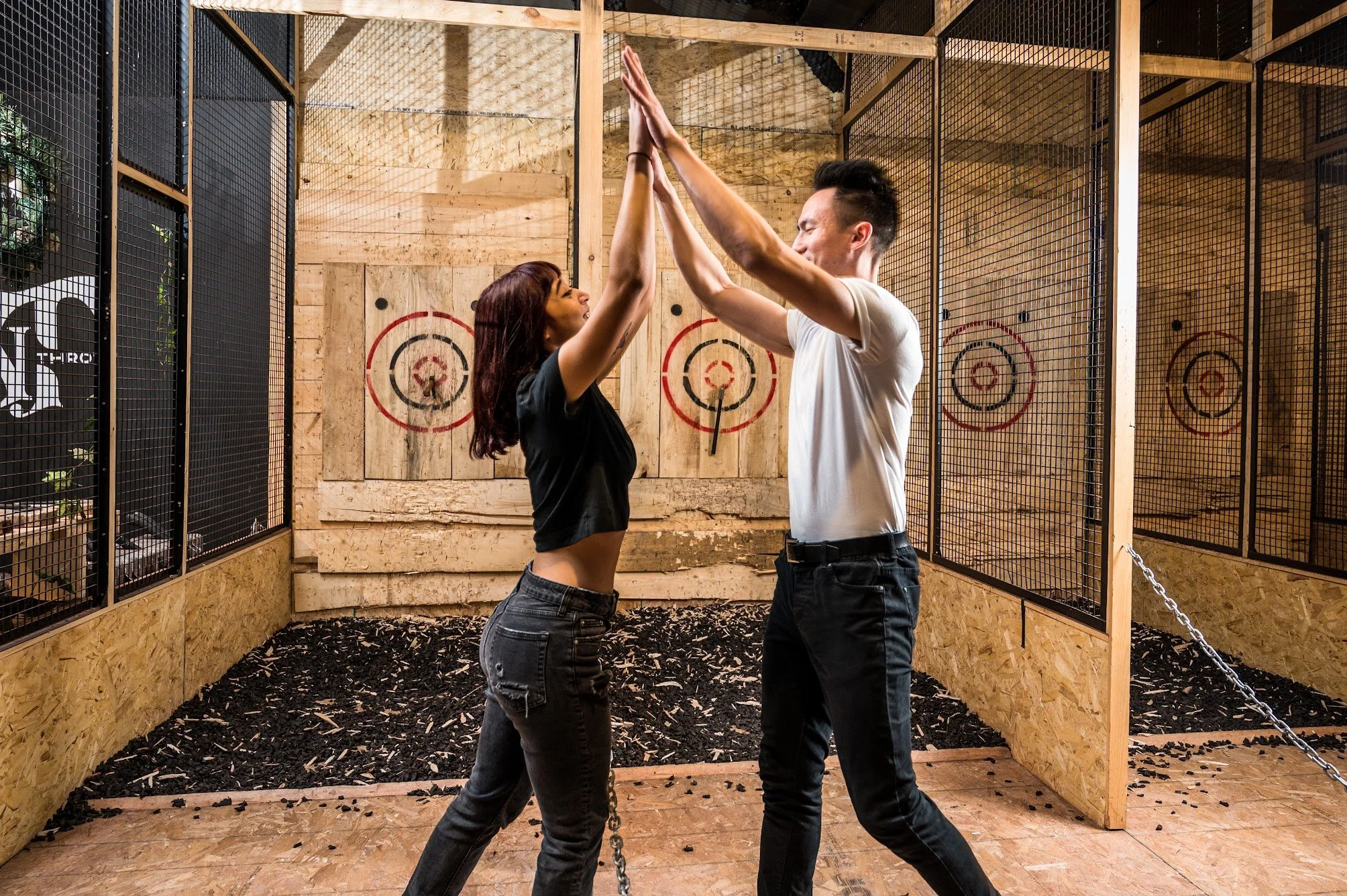 A man and woman high-fiving each other inside a wooden axe-throwing target range.