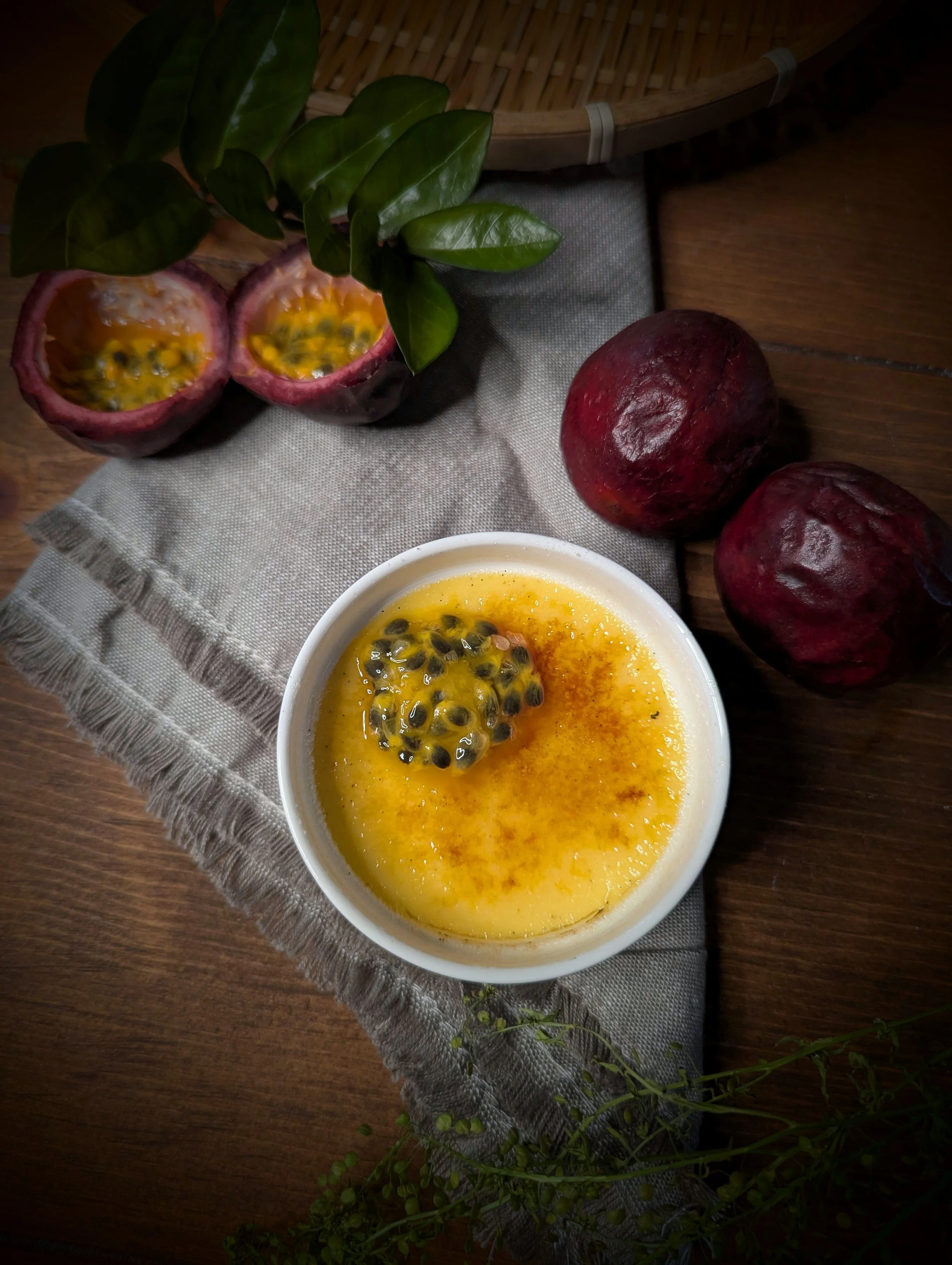 Passion fruit dessert with a passion fruit half on top, surrounded by whole passion fruits, on a linen cloth and wooden table.