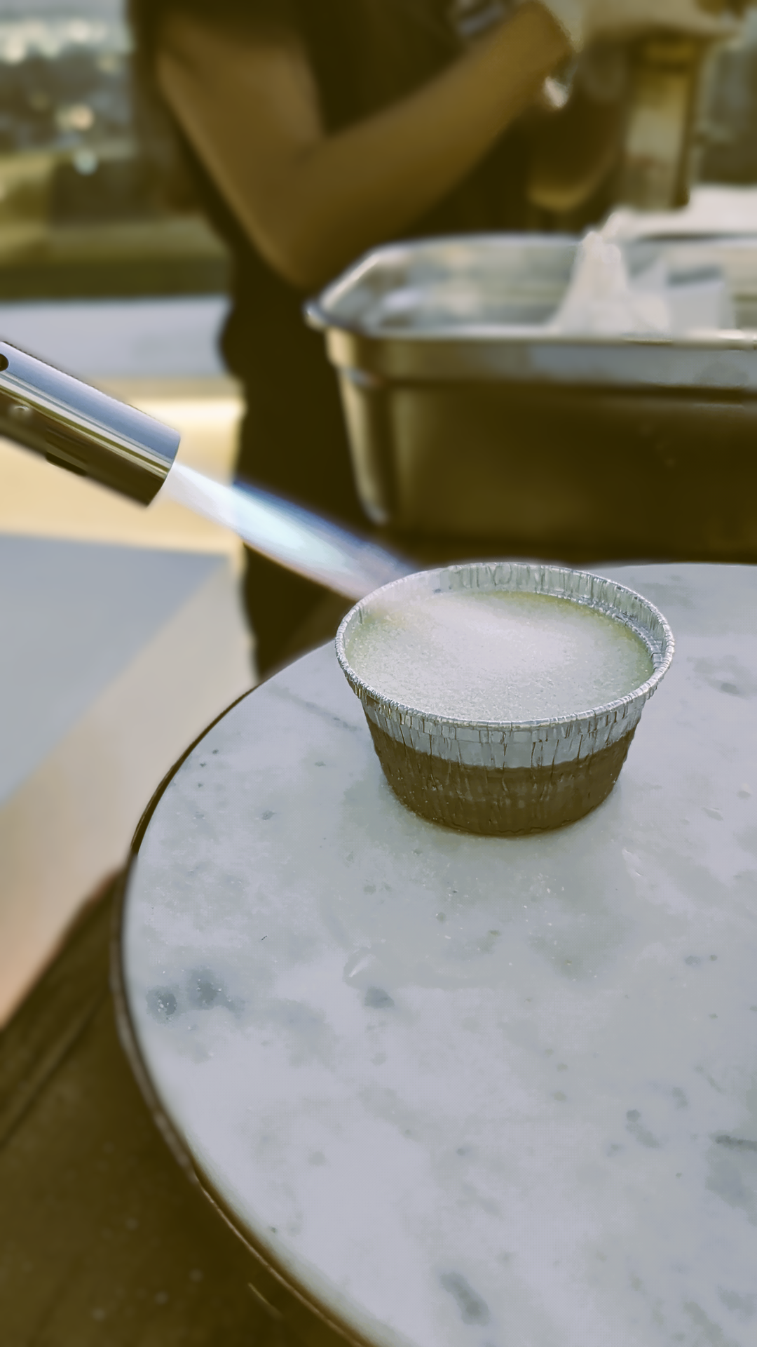 A disposable bowl with a frosty appearance on a ice-covered table, with a person in the background spray painting, and a metal food container nearby.
