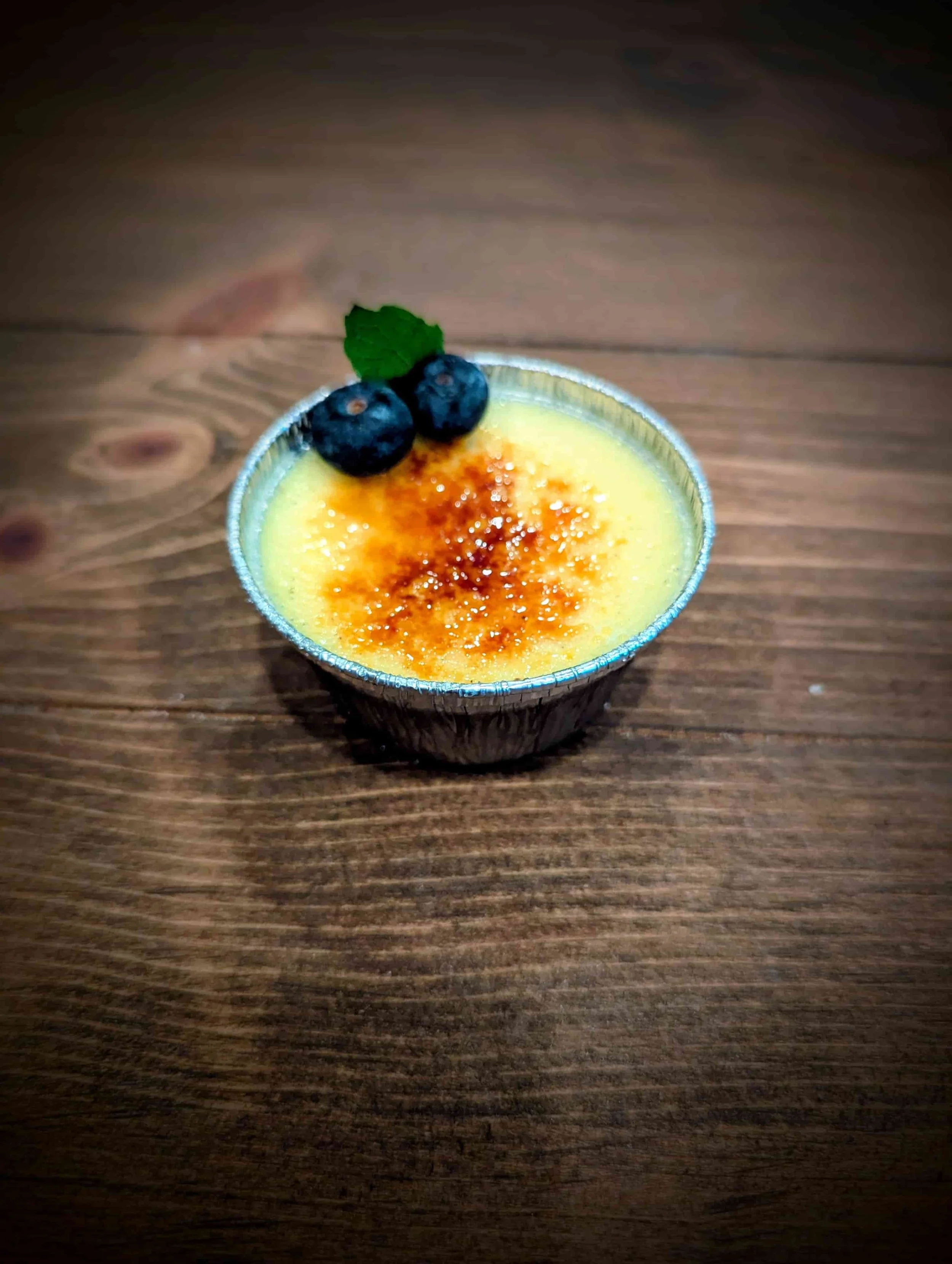 Classic vanilla bean crème brûlée with caramelized sugar topping and fresh blueberries, served for dessert catering in Los Angeles and Orange County