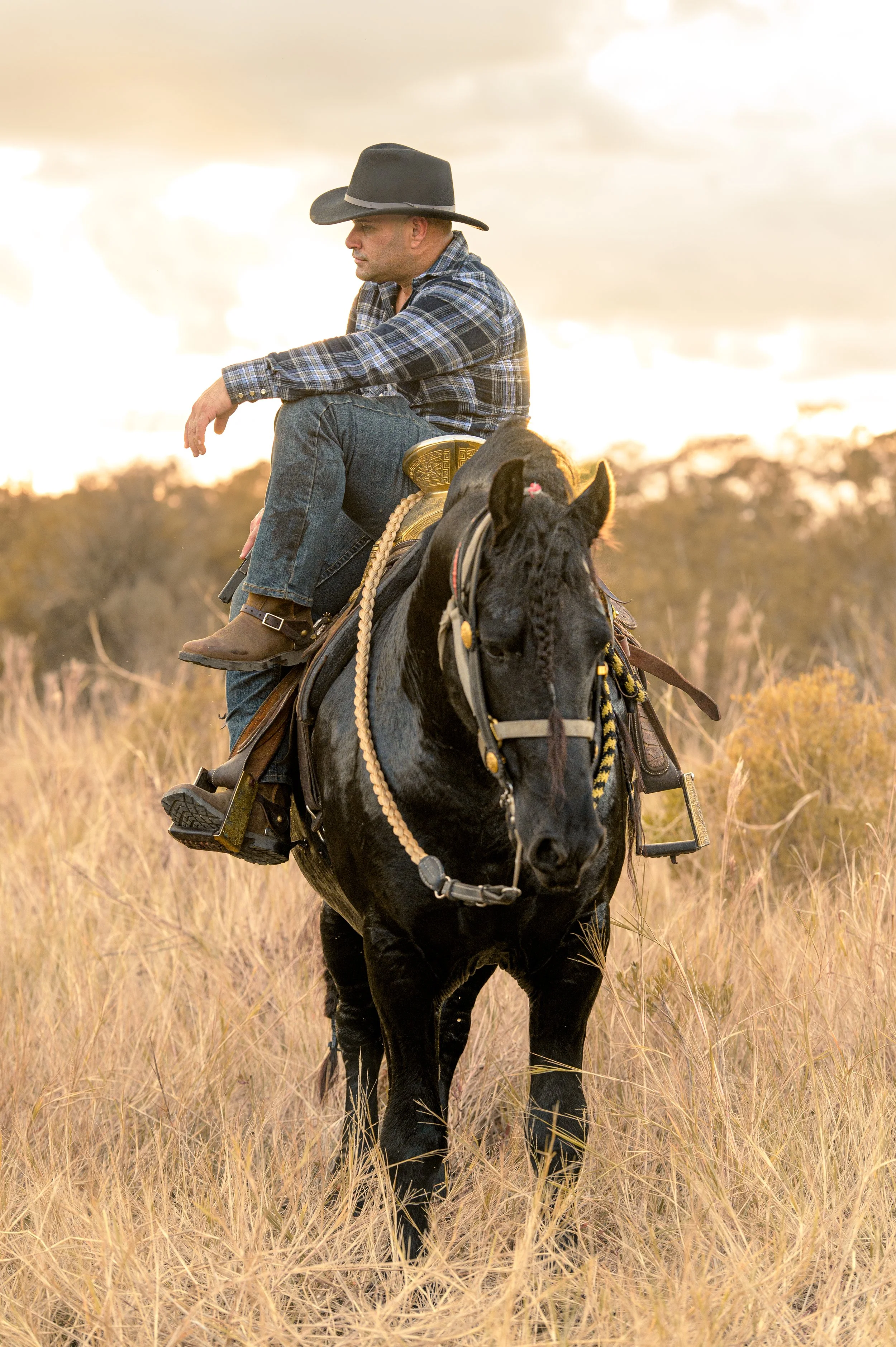 Un hombre montado a caballo en un campo de pasto con cielo nublado al atardecer. Vaqueros Del Pantano.