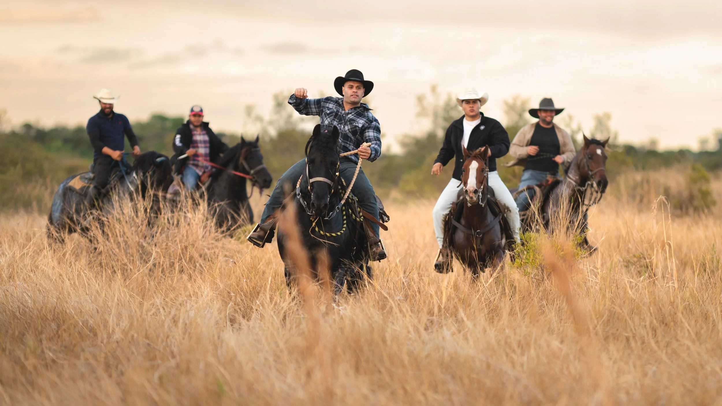 Cinco personas montando caballos en un campo de hierba seca, algunos con sombreros y ropa de campo, disfrutando de una actividad al aire libre. Vaqueros Del Pantano.