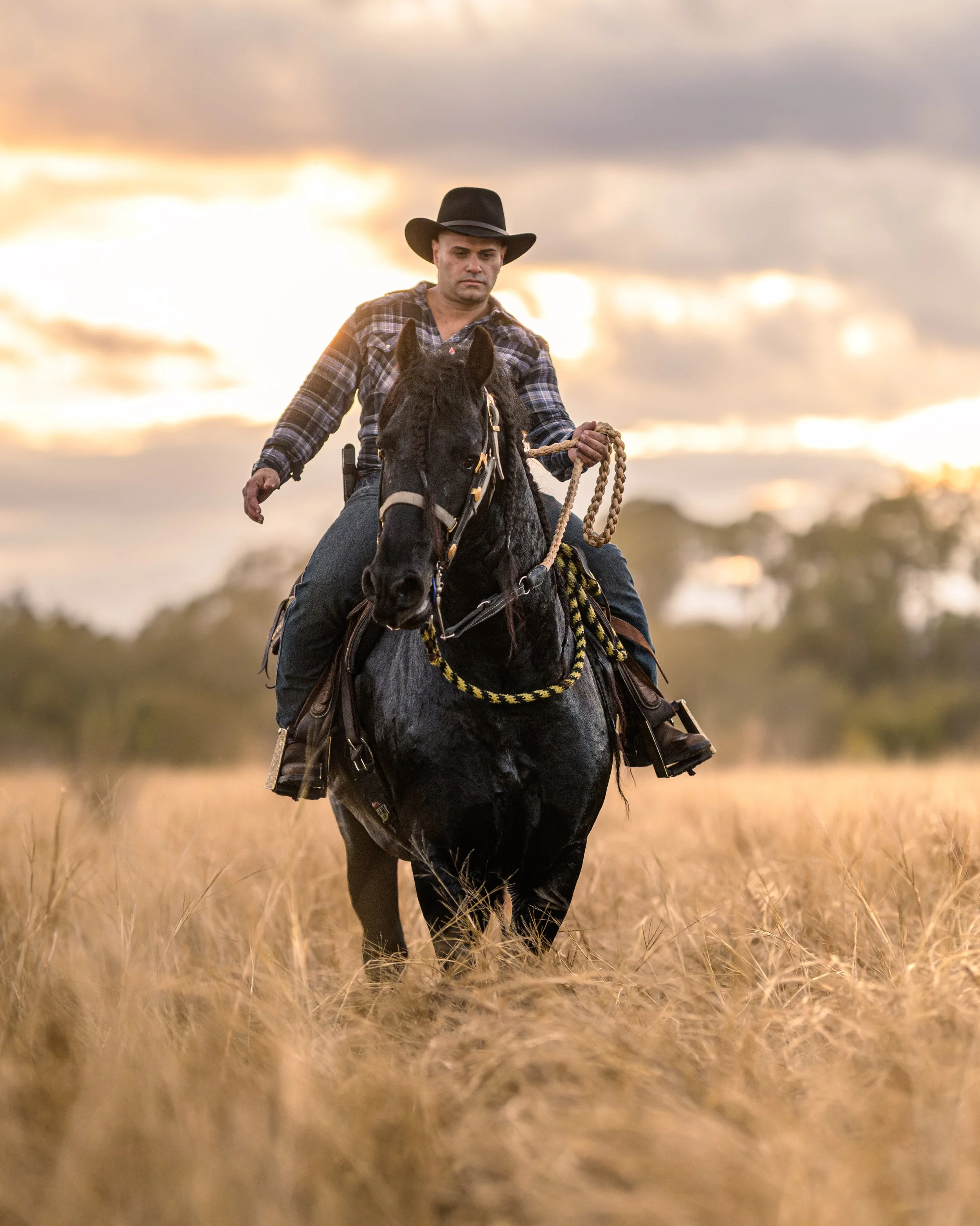 Hombre cabalgando un caballo en un campo con cielo nublado y atardecer. Vaqueros Del Pantano.