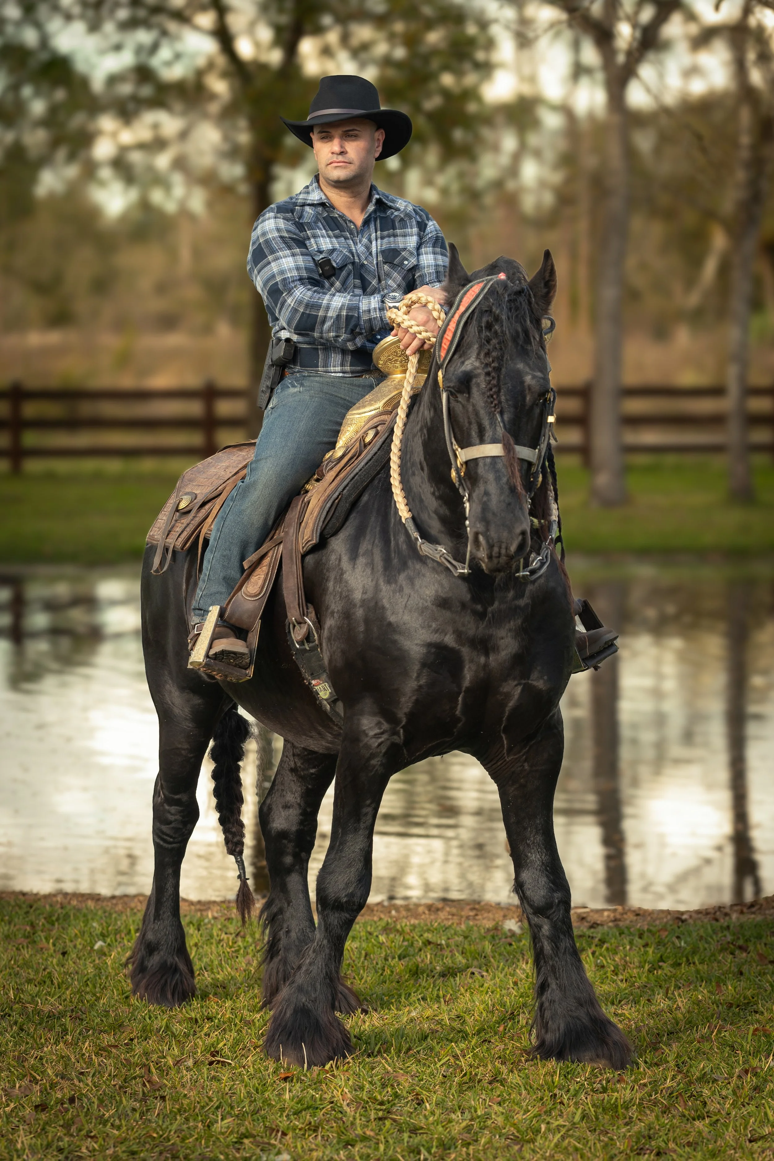 Luis Aqino montado a caballo, con sombrero y ropa de vaquero, en un ambiente al aire libre con árboles y agua. Vaqueros Del Pantano.