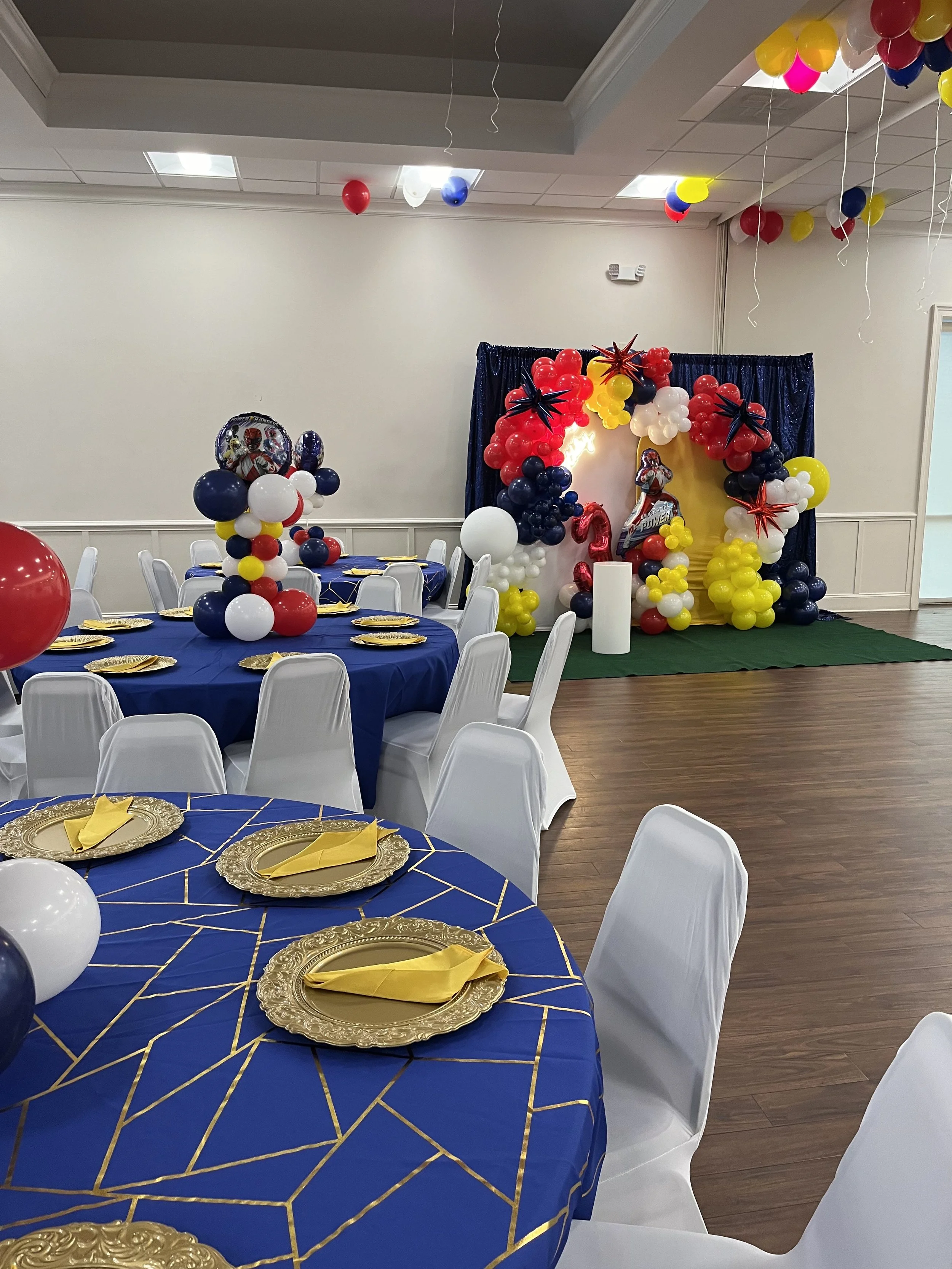 Party room decorated with colorful balloons, featuring a backdrop with balloons and a figure of a woman in a red and white dress for celebration.