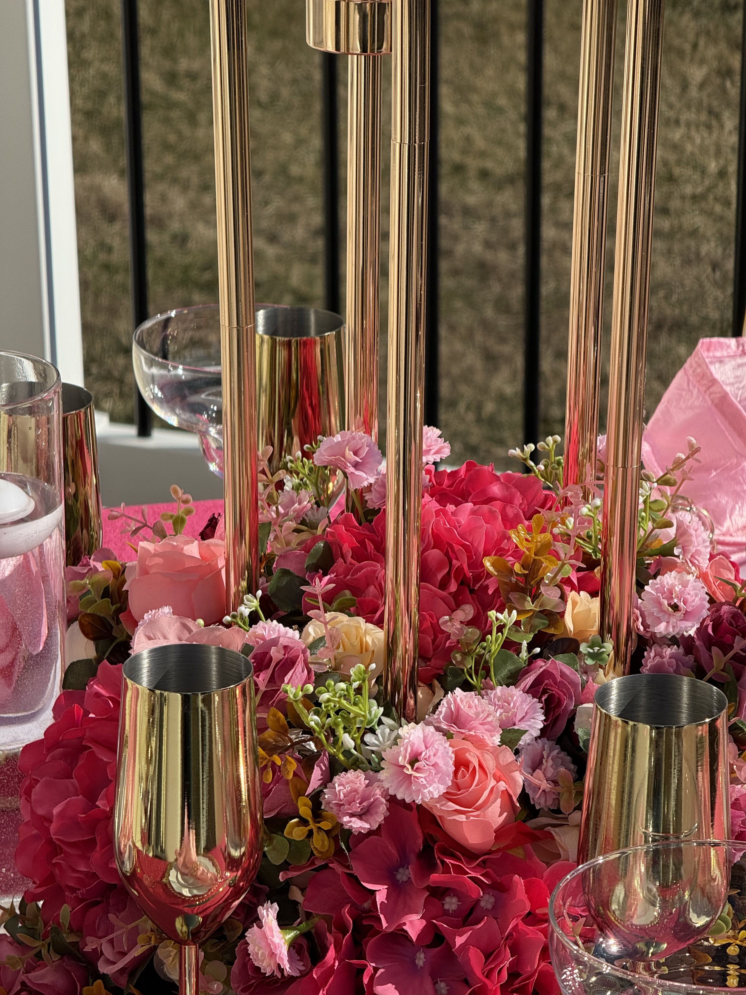 Close-up of a floral centerpiece with pink and red flowers, surrounded by gold and glass candle holders on a table.
