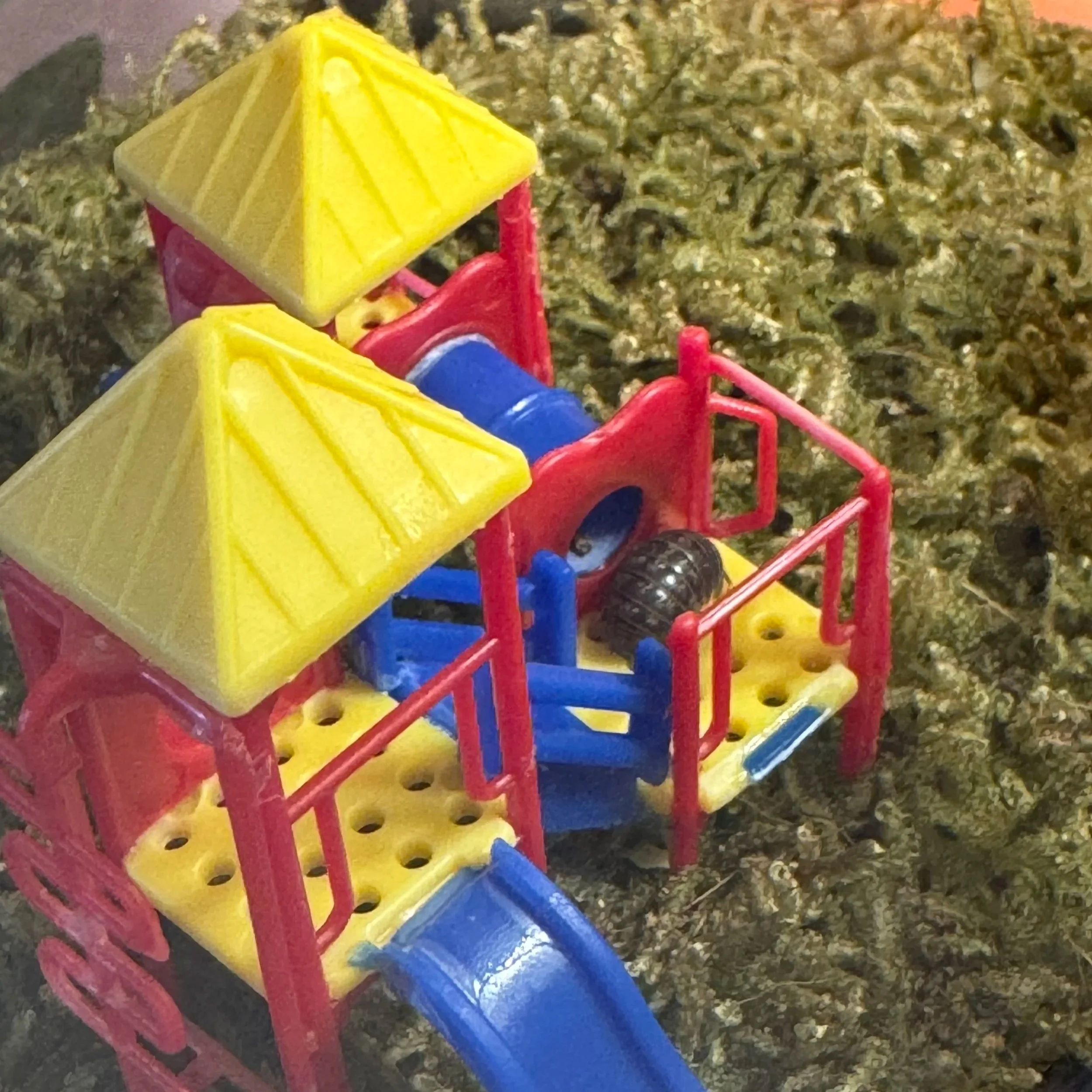 Close-up of a colorful children's play structure featuring a red rail, blue pole, yellow steps, and green ground cover. a roly poly playground