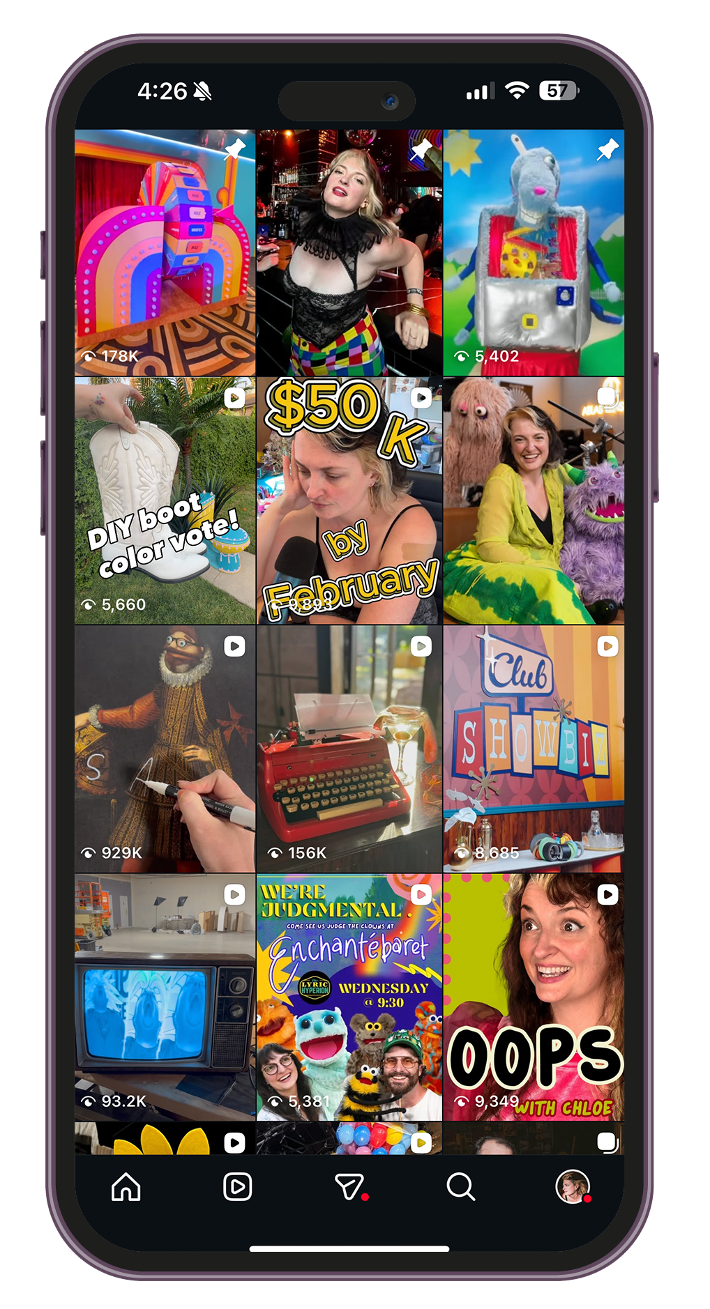 A smartphone screen displaying a grid of YouTube video thumbnails, showing various colorful and quirky images including a rainbow-themed arcade machine, a woman at a party, a puppet, a typewriter, a TV screen, and a group of people with puppets.