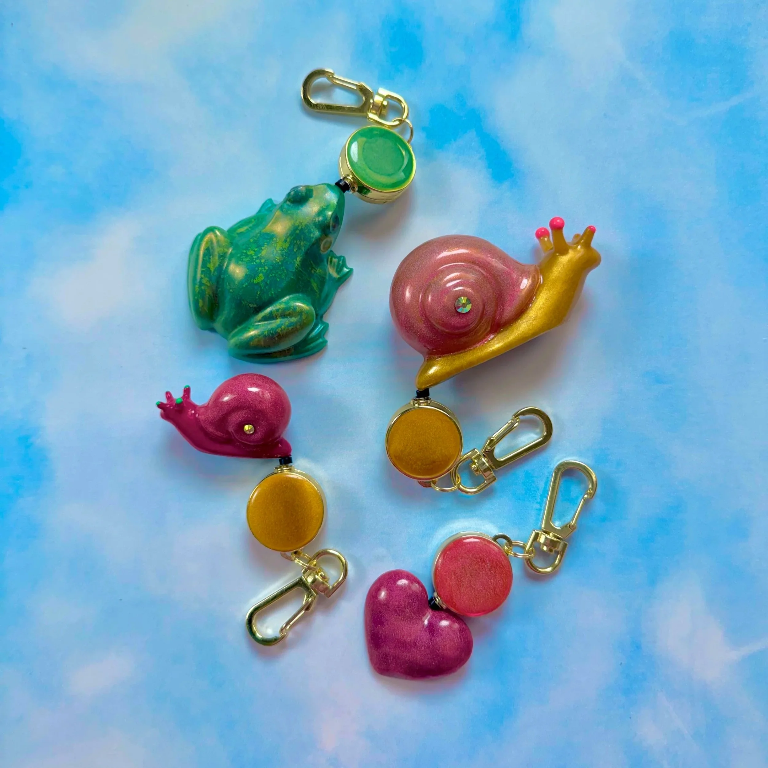 Keychain featuring a green dolphin, a pink snail, and a pink octopus, attached to gold-colored clips and rings, resting on a light blue background.