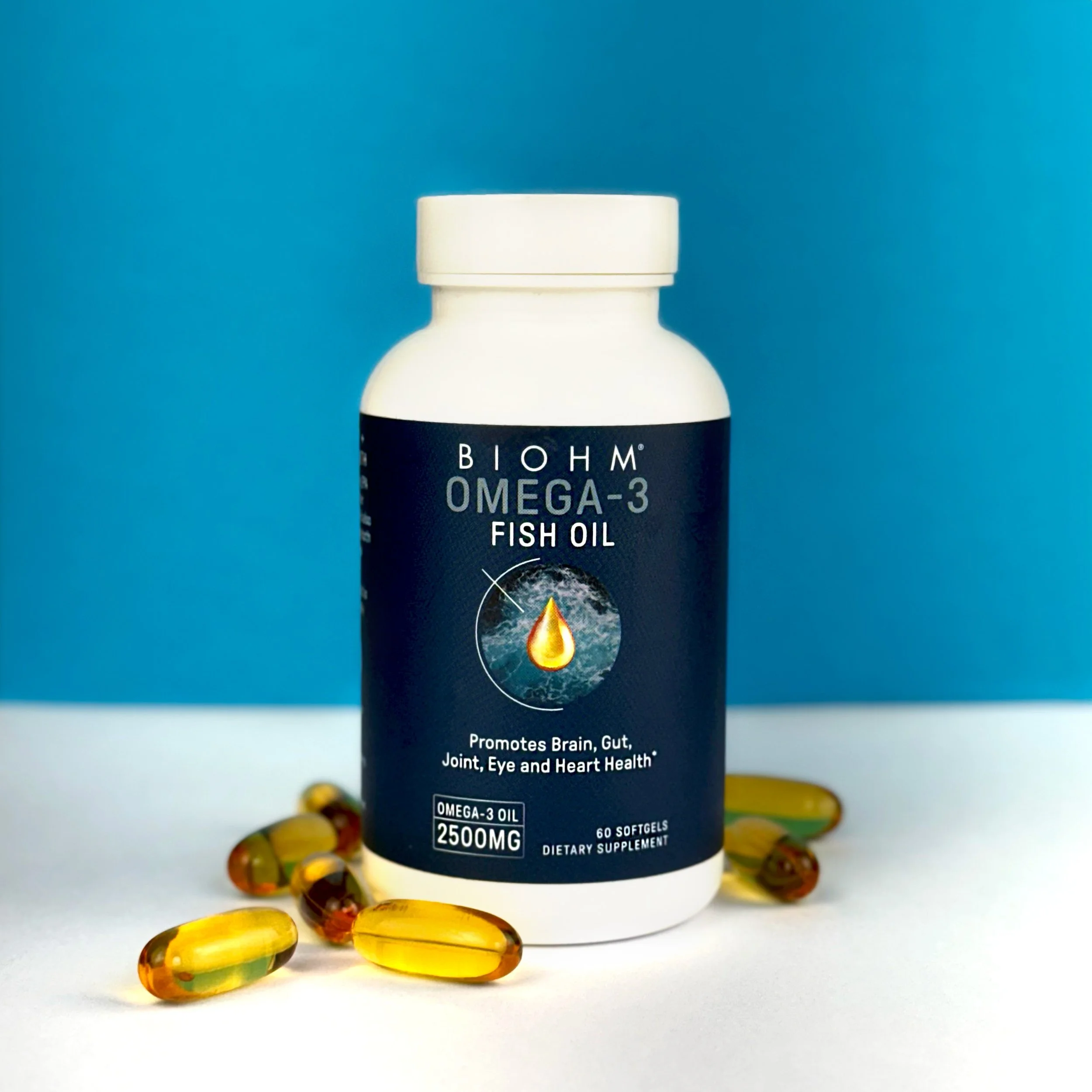 A white bottle of BIOHM Omega-3 Fish Oil dietary supplement with a black label, surrounded by yellow and brown softgel capsules, against a blue background.