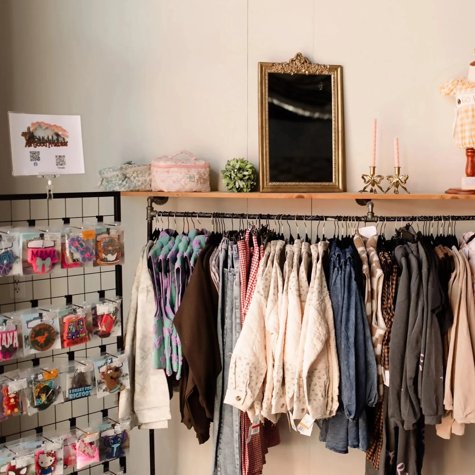 Clothing store display with a variety of jackets and shirts on a rack, decorative mirror, candles, and accessories.