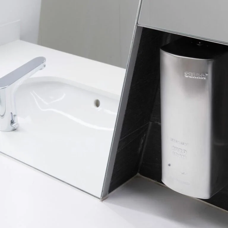 A soap dispenser mounted on a wall with a sink and faucet in a restroom.
