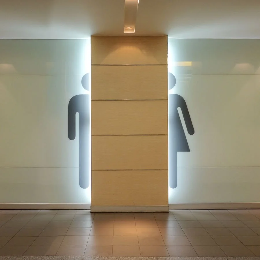 Restroom signs visible behind a beige wall with soft lighting and tiled flooring.