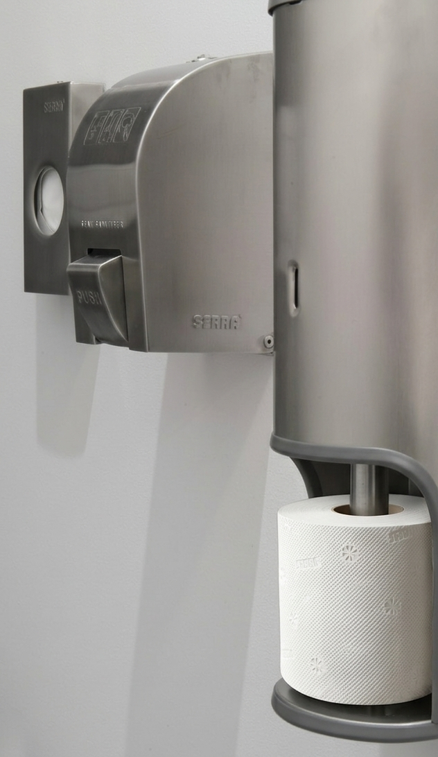 A wall-mounted toilet roll dispenser with a roll of toilet paper below it in a restroom or washroom.