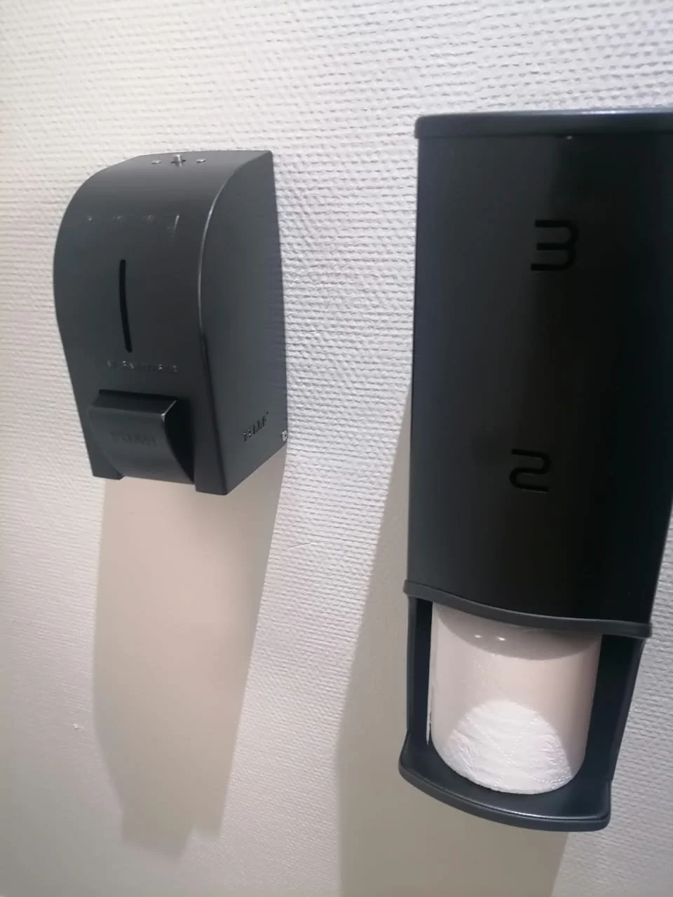 wall-mounted sanitizer dispensers containing sanitizer and the black dispenser with a white tissue inside.