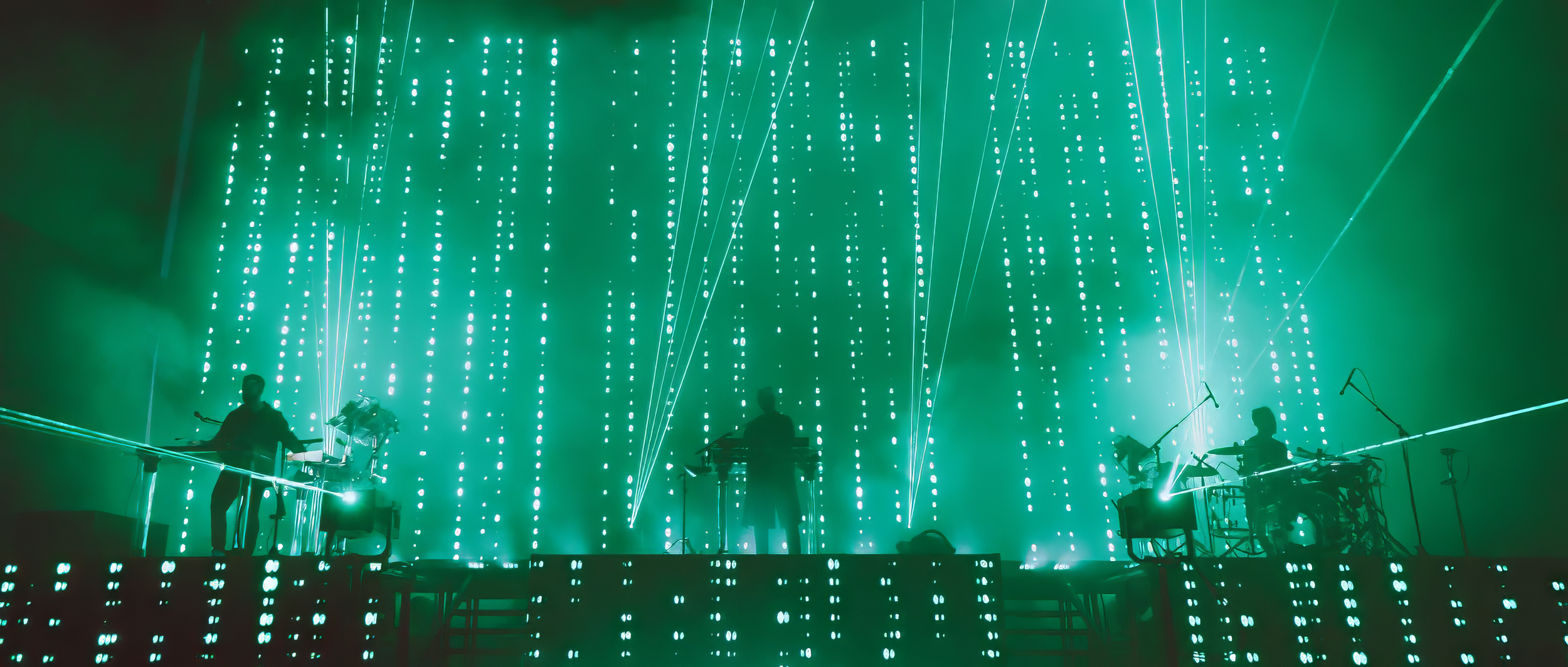 Musicians performing beneath green laser light and large-format screens