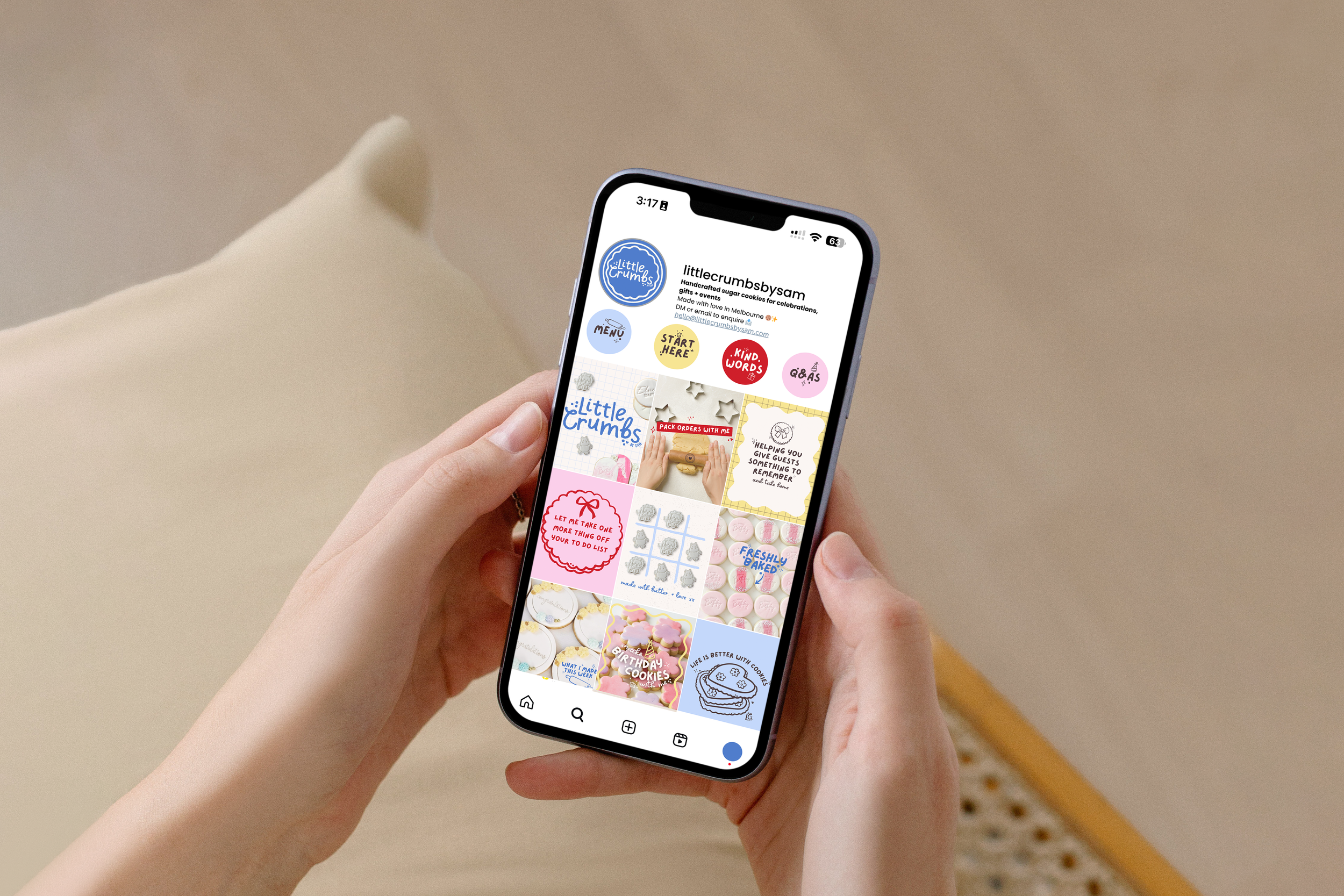 A person holding a smartphone displaying a website for Little Crumbs, a business that makes handcrafted sugar cookies for celebrations, with various colorful cookie designs on the screen.