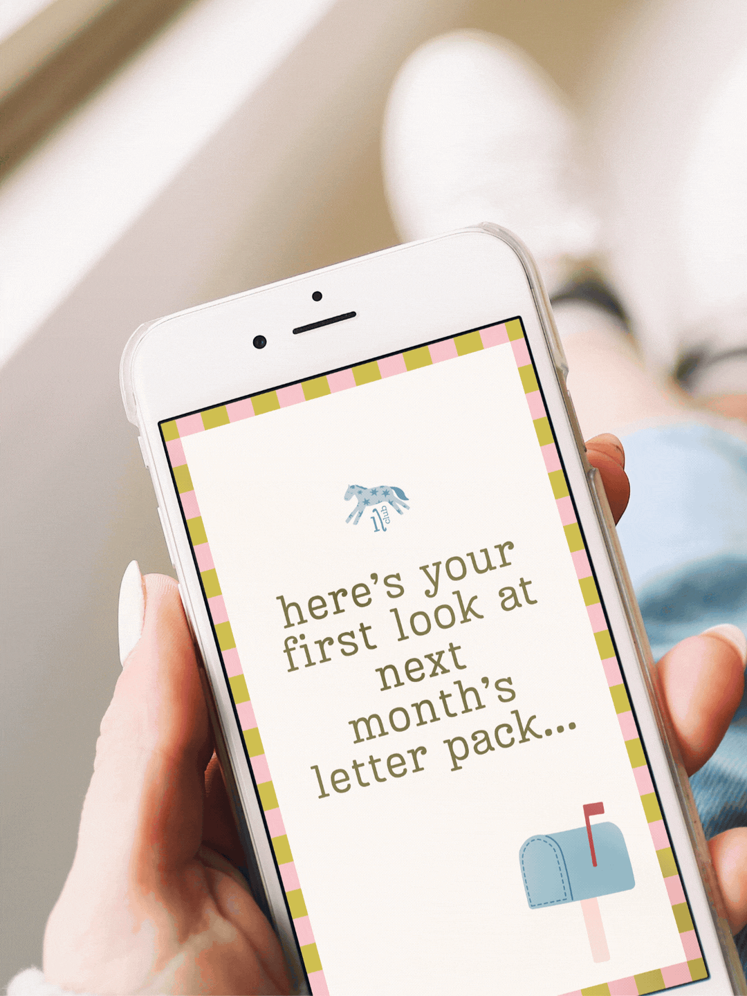 A person holding a smartphone displaying a message that says, "here's your first look at next month's letter pack..." with a small illustration of a mailbox at the bottom right corner.