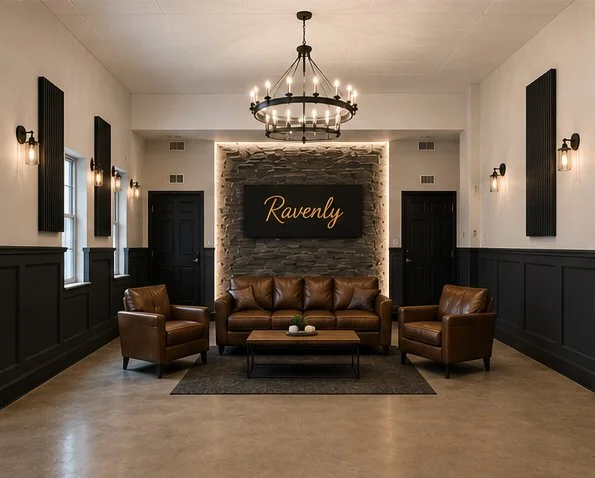 A modern living room with a leather sofa and two matching armchairs centered around a low coffee table, a stone accent wall with a sign that reads "Ravenly," and a large chandelier hanging from the ceiling.