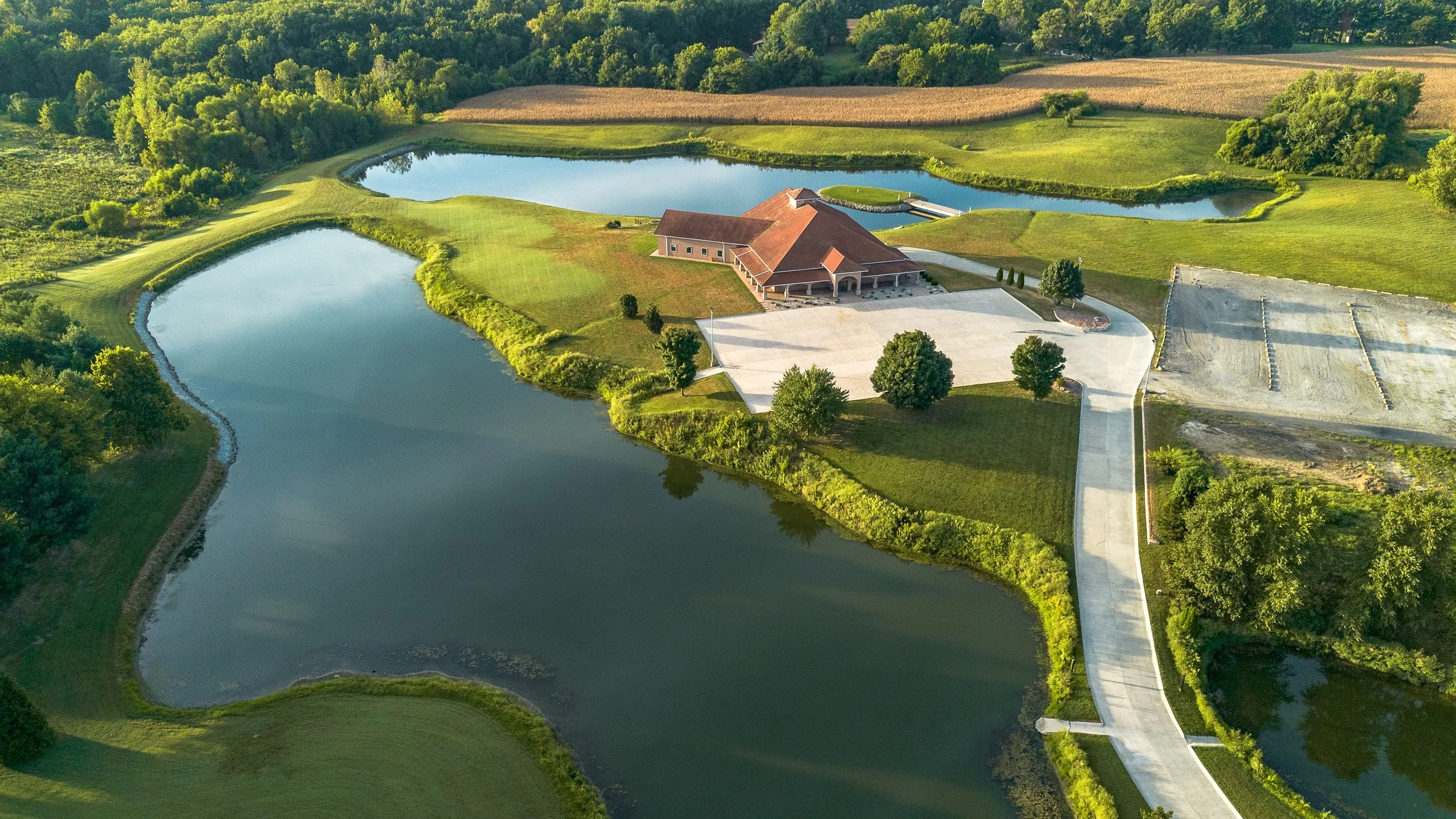 Aerial view of a rural landscape with a water feature, a building, a parking area, and surrounding greenery.