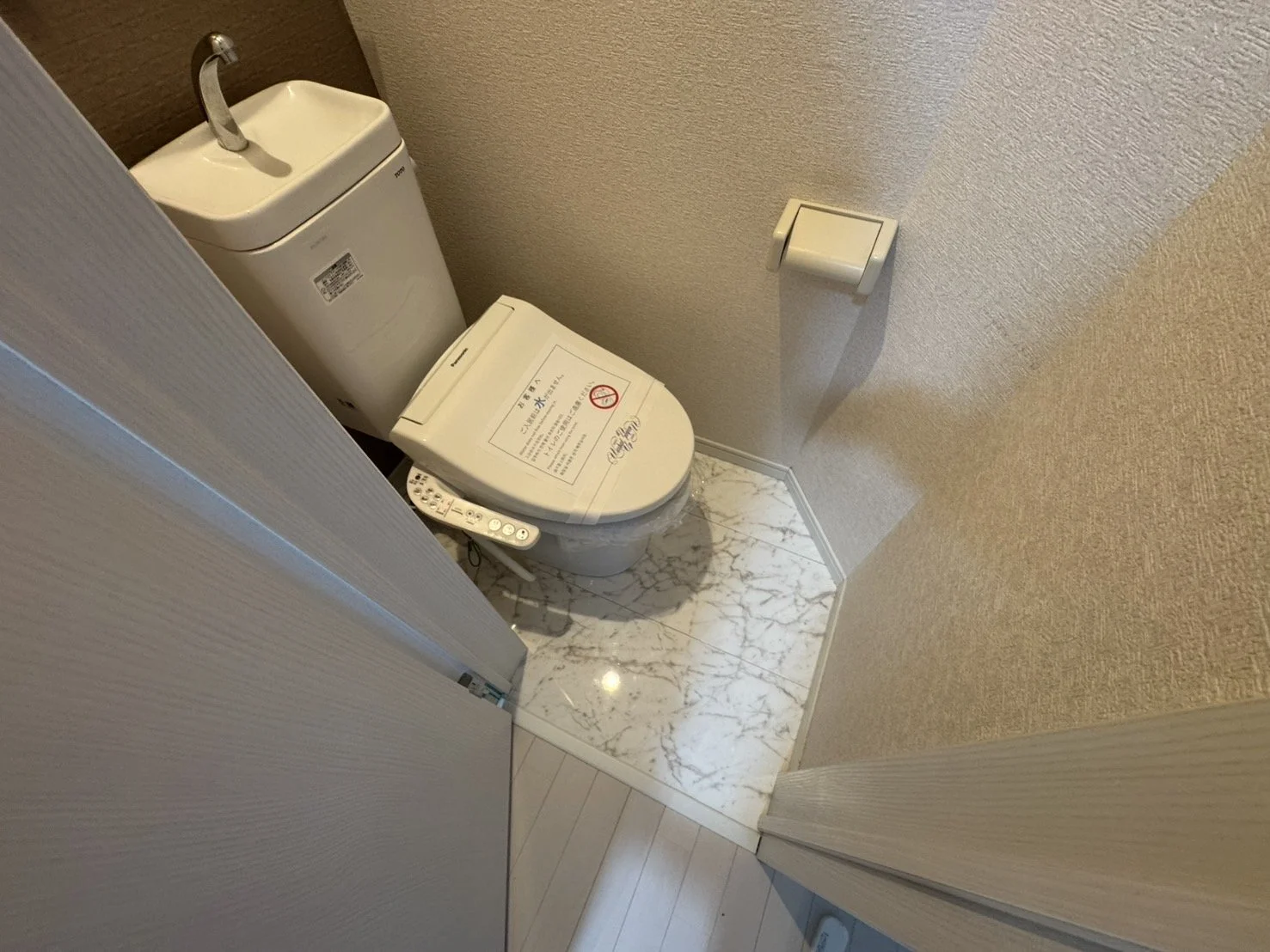 トイレの便座とトイレットペーパーのホルダーがある狭いトイレ空間。