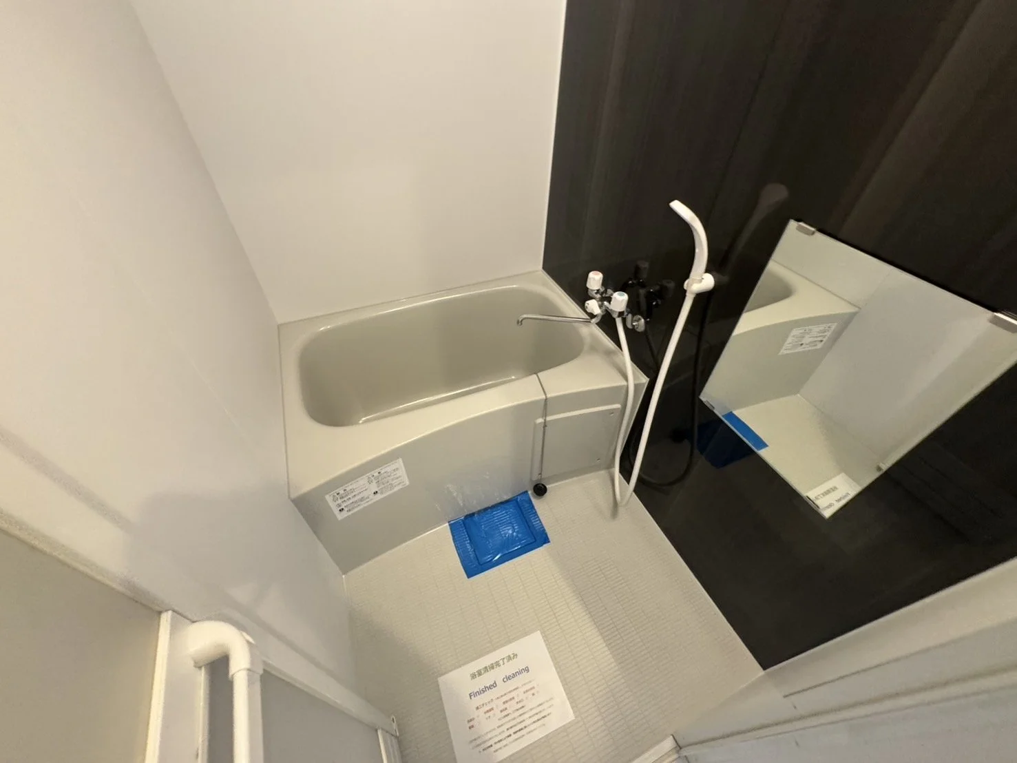 小さな浴槽とシャワー付きのバスルームの interior には鏡と白いタイルの床がある