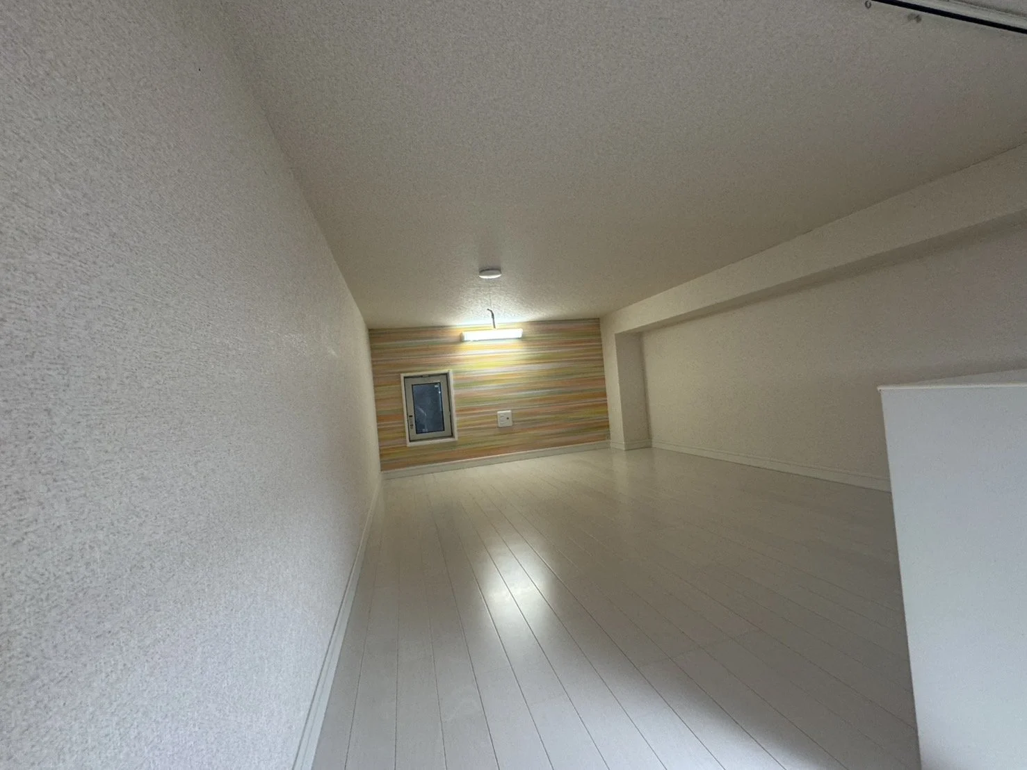 空の屋根裏部屋、白い壁と木製の床、壁の一部に横縞模様の壁紙、窓と照明付きです。