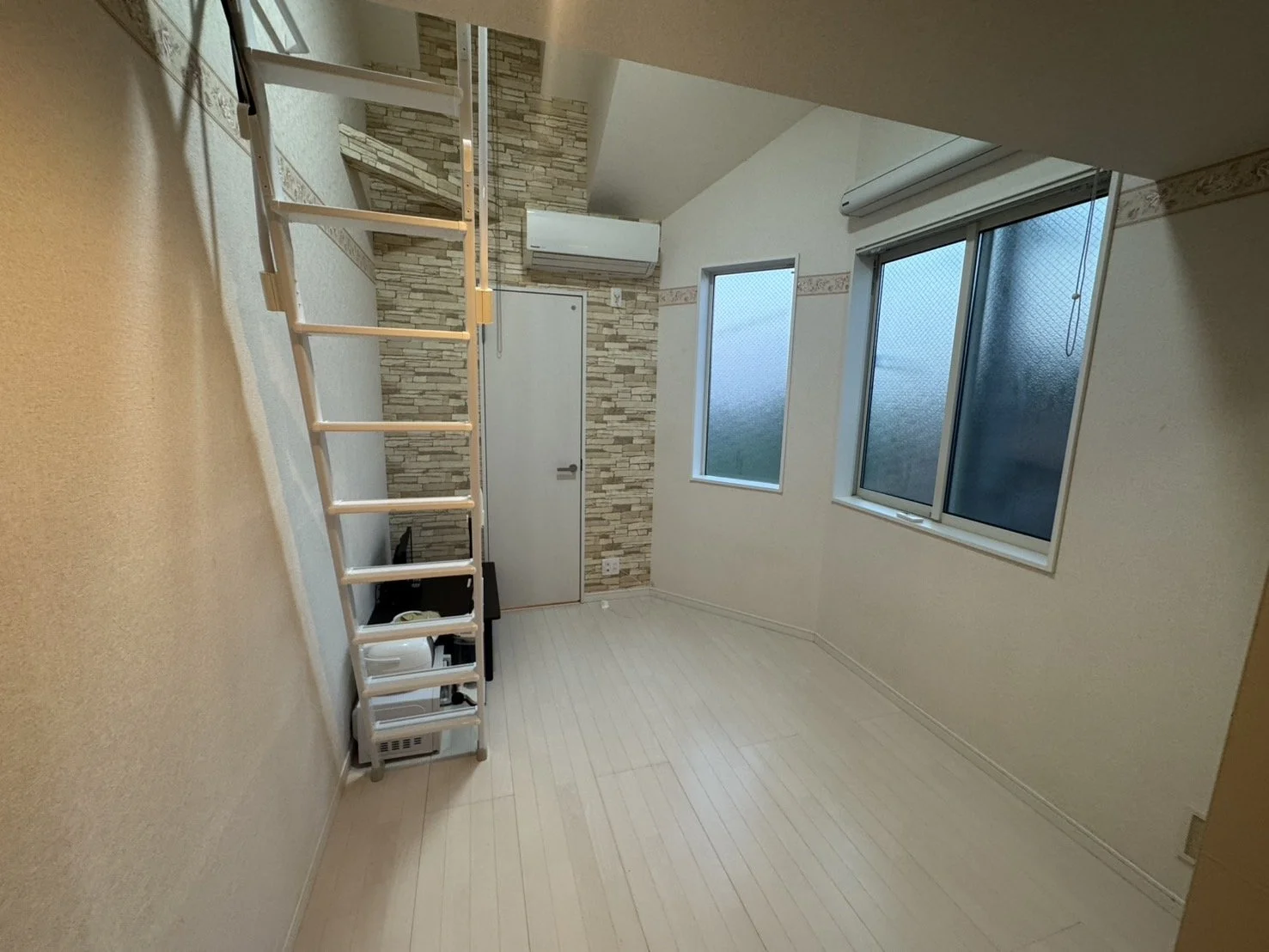 空の部屋。白い壁と木製の床、窓とエアコンがある。