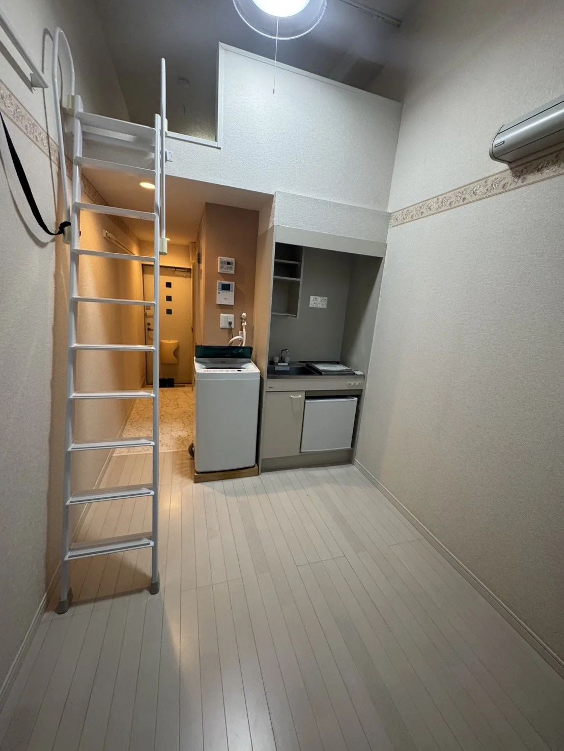 小さなキッチンと洗濯機のある室内、ロフトに登る階段とドアが見える