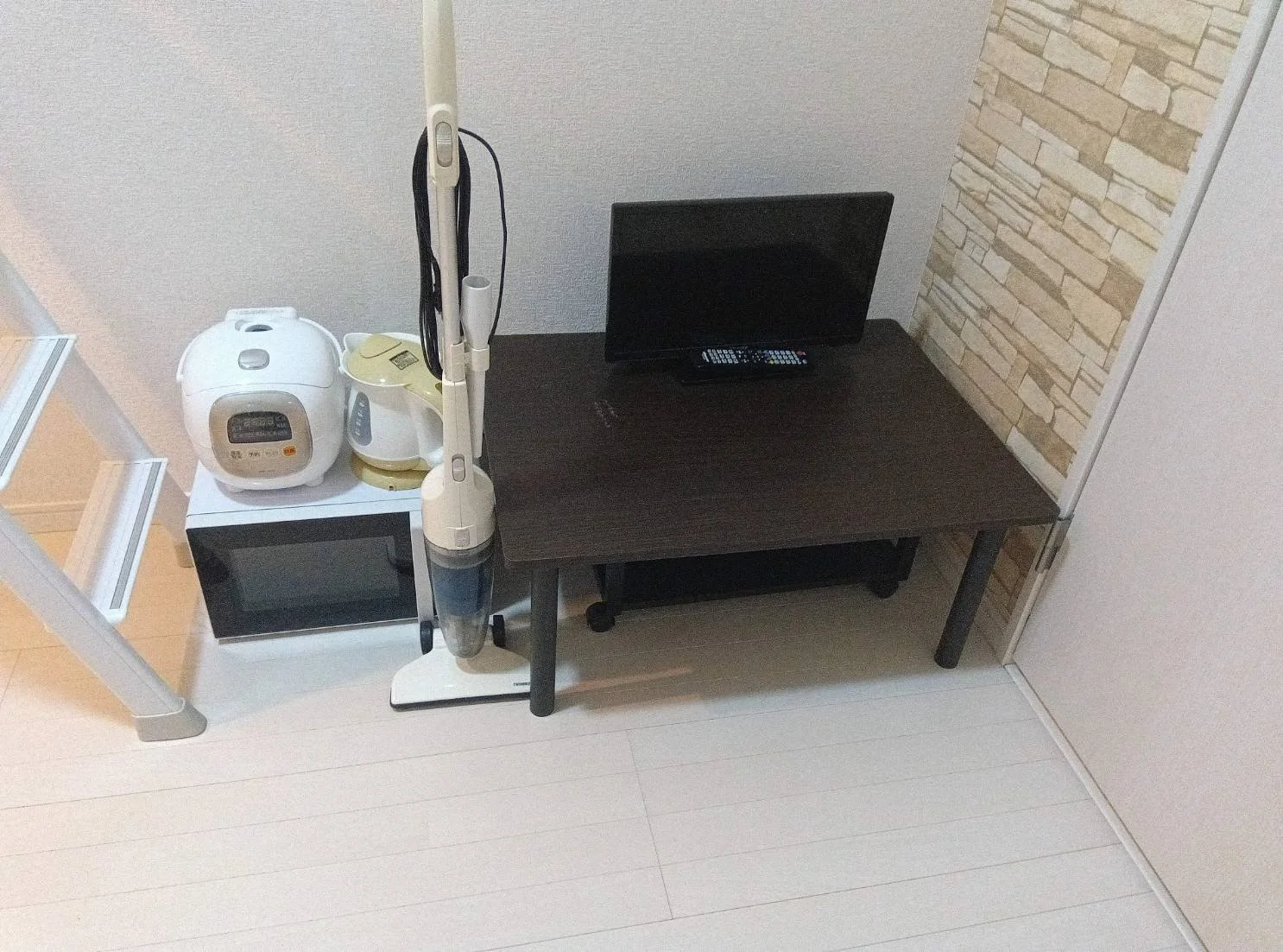 リビングの一角にテレビ台とテレビ、電子レンジ、炊飯器、掃除機が配置されている