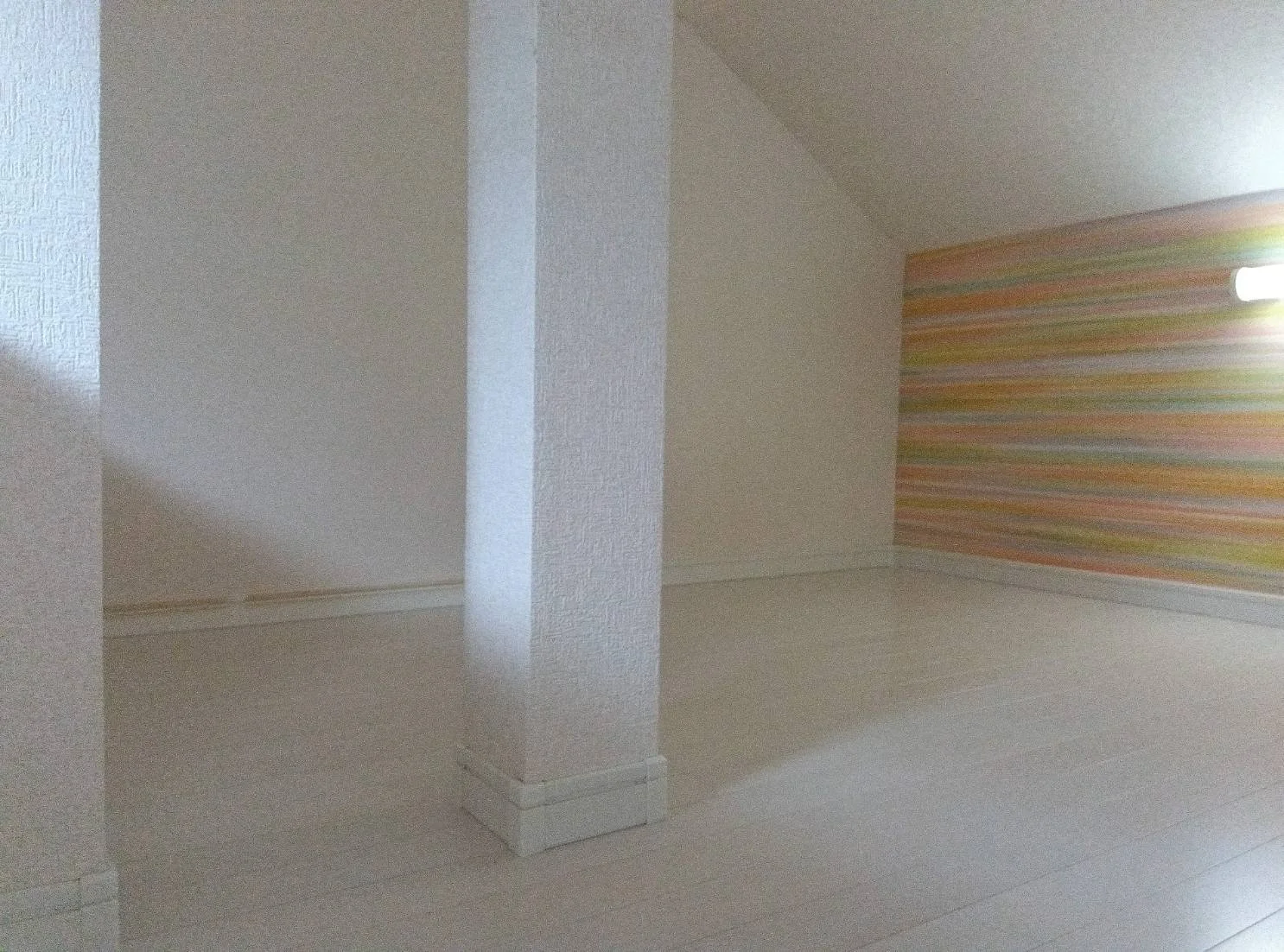 白い壁と柱、カラフルなストライプの壁紙がある部屋の角の写真