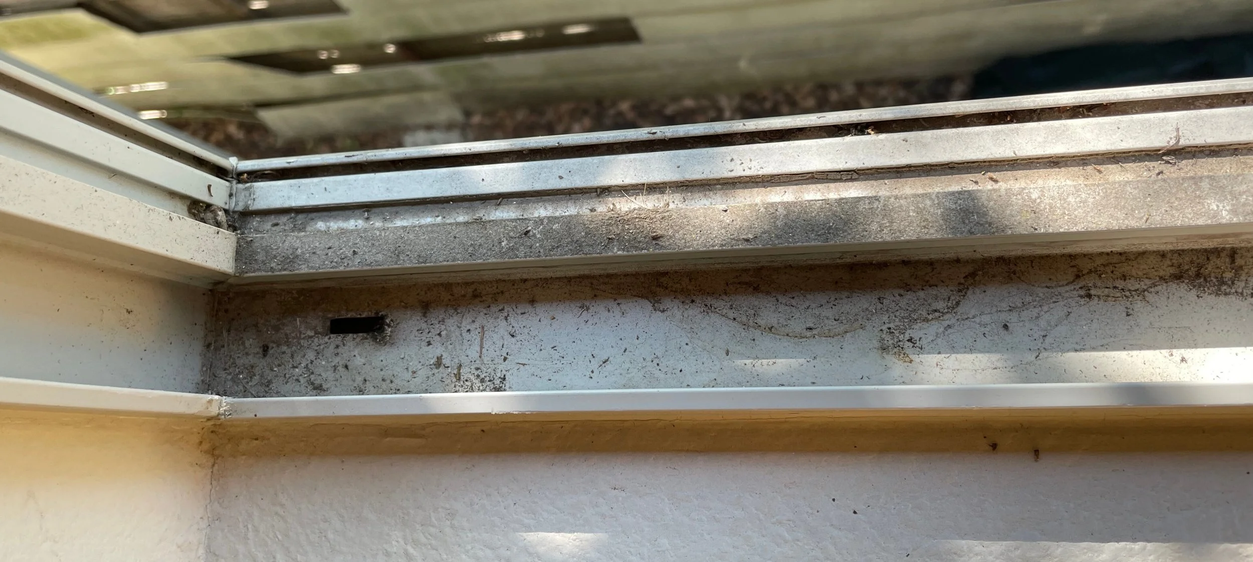 An image showing a close-up view of a window sill and a sliding window track, both covered in dust, dirt, and debris.