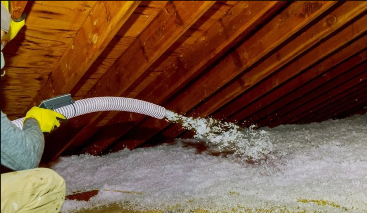 Person spraying insulation material into an attic space through a flexible hose.