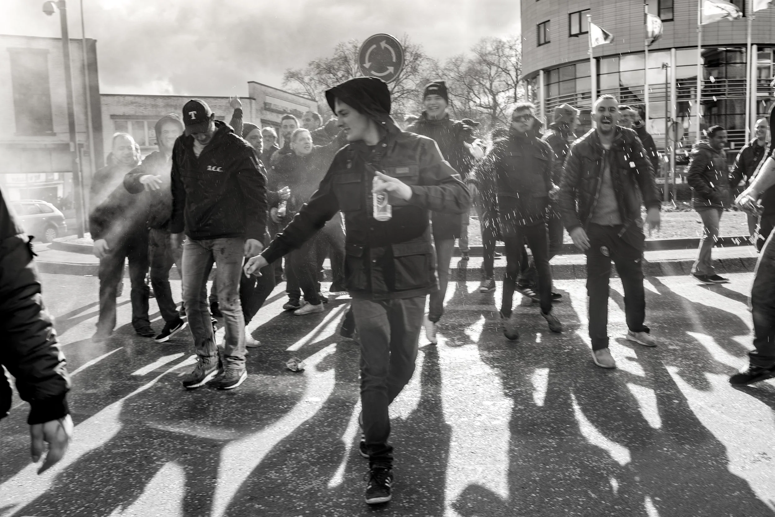 Een groep mensen die water spuiten en plezier maken op straat op een zonnige dag, met moderne gebouwen op de achtergrond.