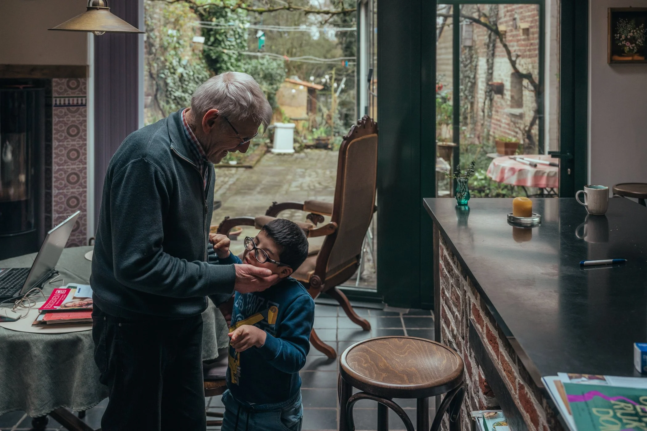 Opa en kleinzoon in de keuken, opa knuffelt de jongen die opkijkt en lachend is.