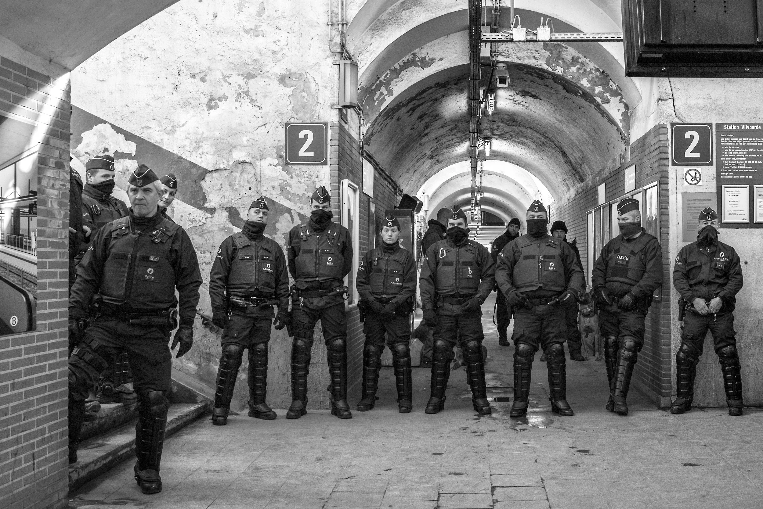 Tien politieagenten in uniform en gezichtsbedekking staan in een tweeluik onder een tunnel in een stad.