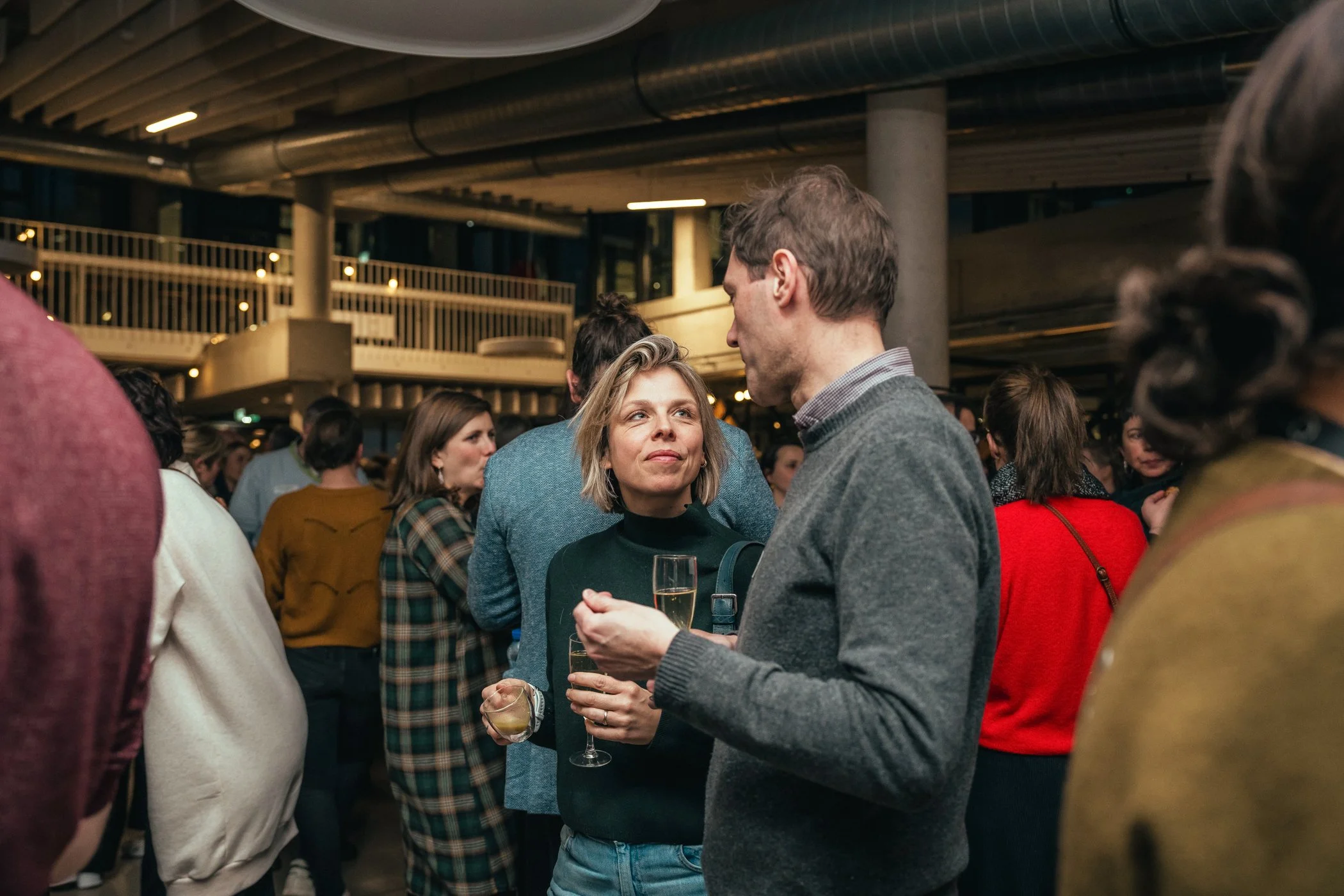 Mensen die praten op een druk feestje of netwerkevent, in een grote moderne ruimte met industriële architectuur.