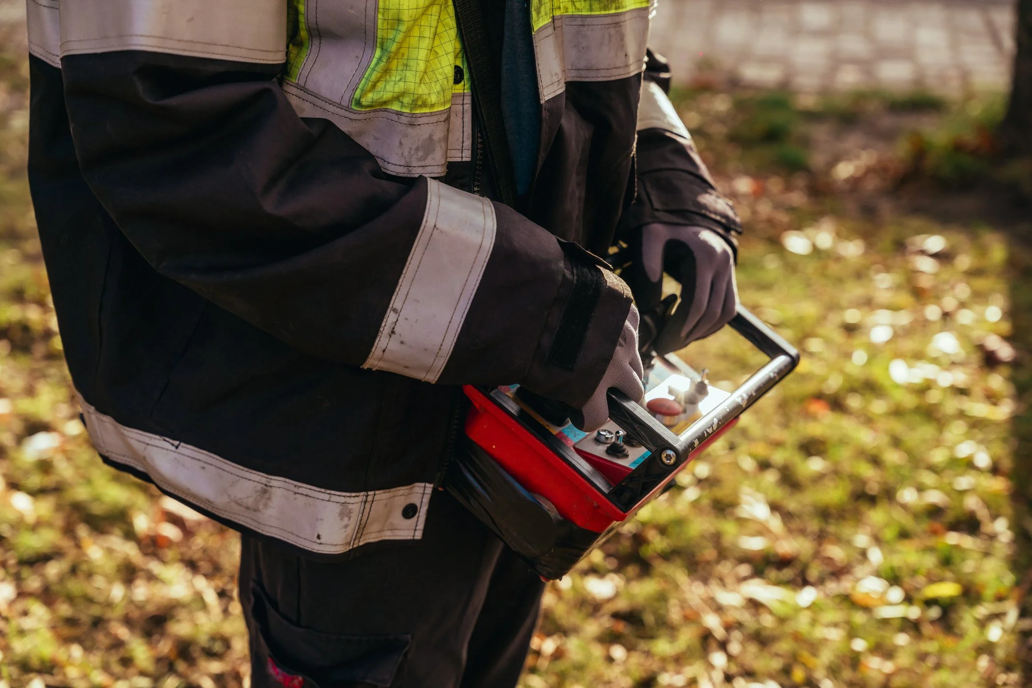 Persoon in een werkjas die een meetinstrument vasthoudt in een bos met bladeren op de grond.