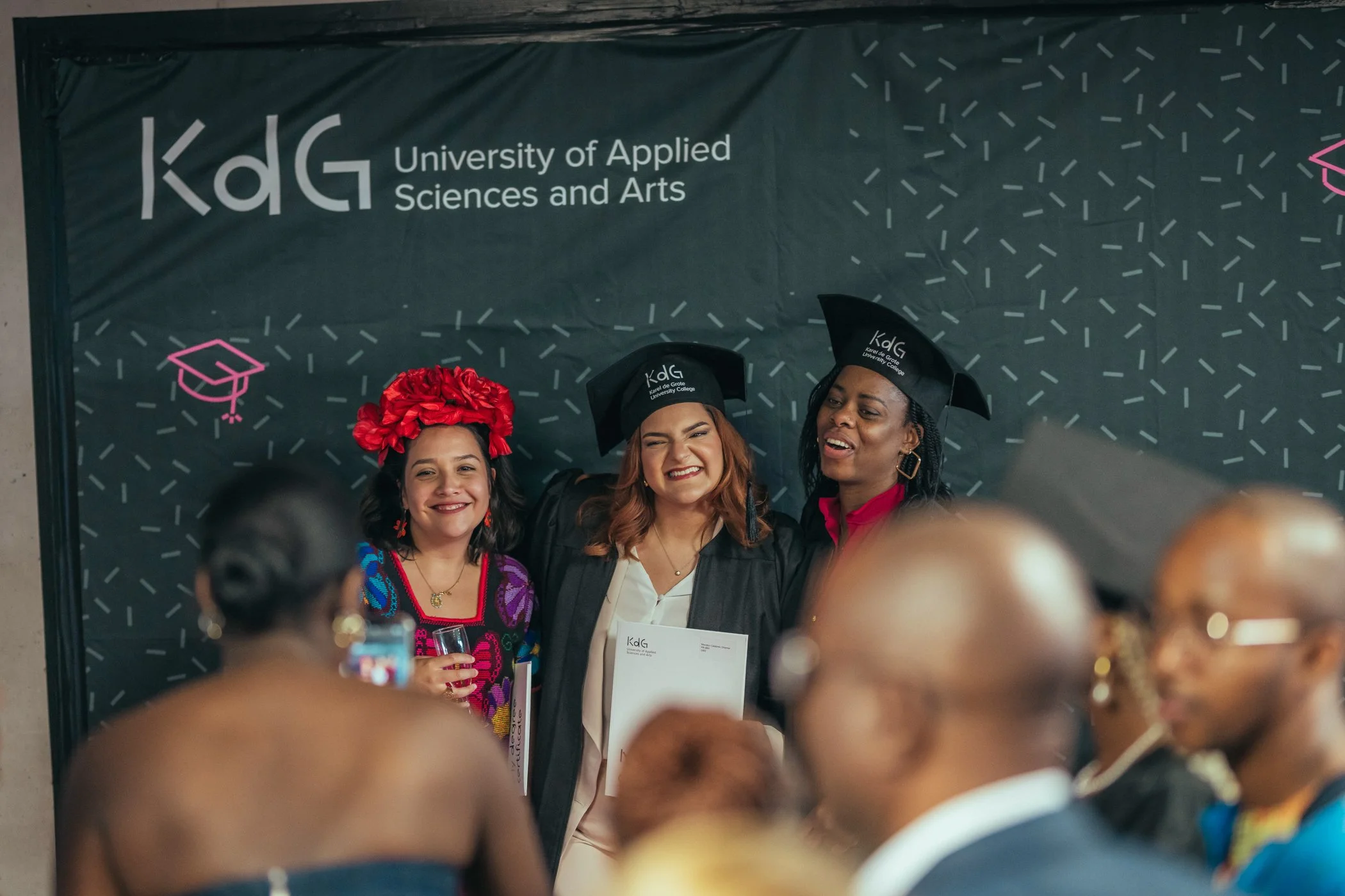 Drie vrouwelijke afgestudeerden in academische kleding en hoed, lachend en poseren voor een groepsfoto tijdens een diploma-uitreiking bij de University of Applied Sciences and Arts (KaDg).