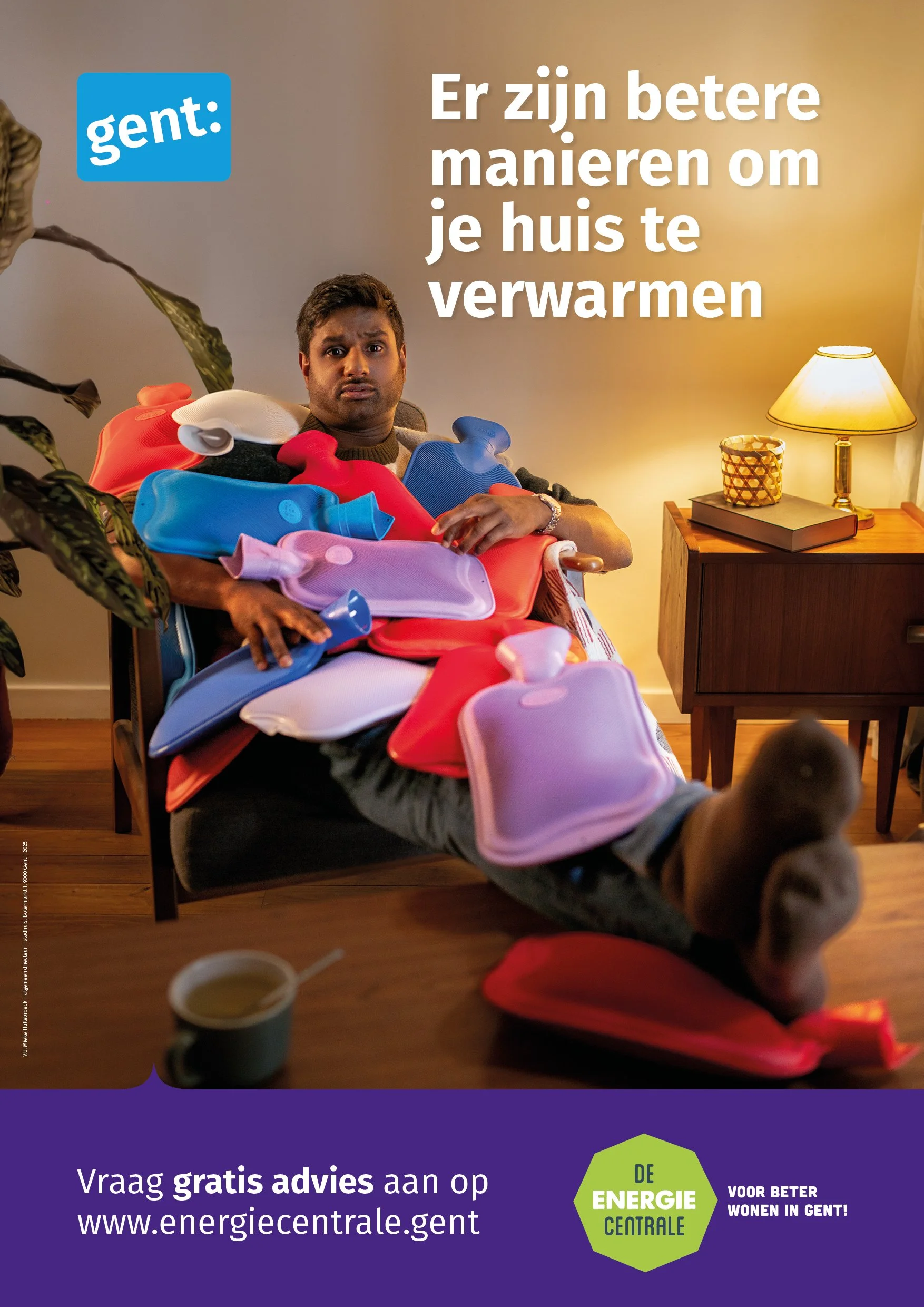 Man zit op een bank met meerdere warmwaterkruiken op schoot, in een warme woonkamer, met een leeslamp en planten op de achtergrond, terwijl hij er verbaasd uitziet.