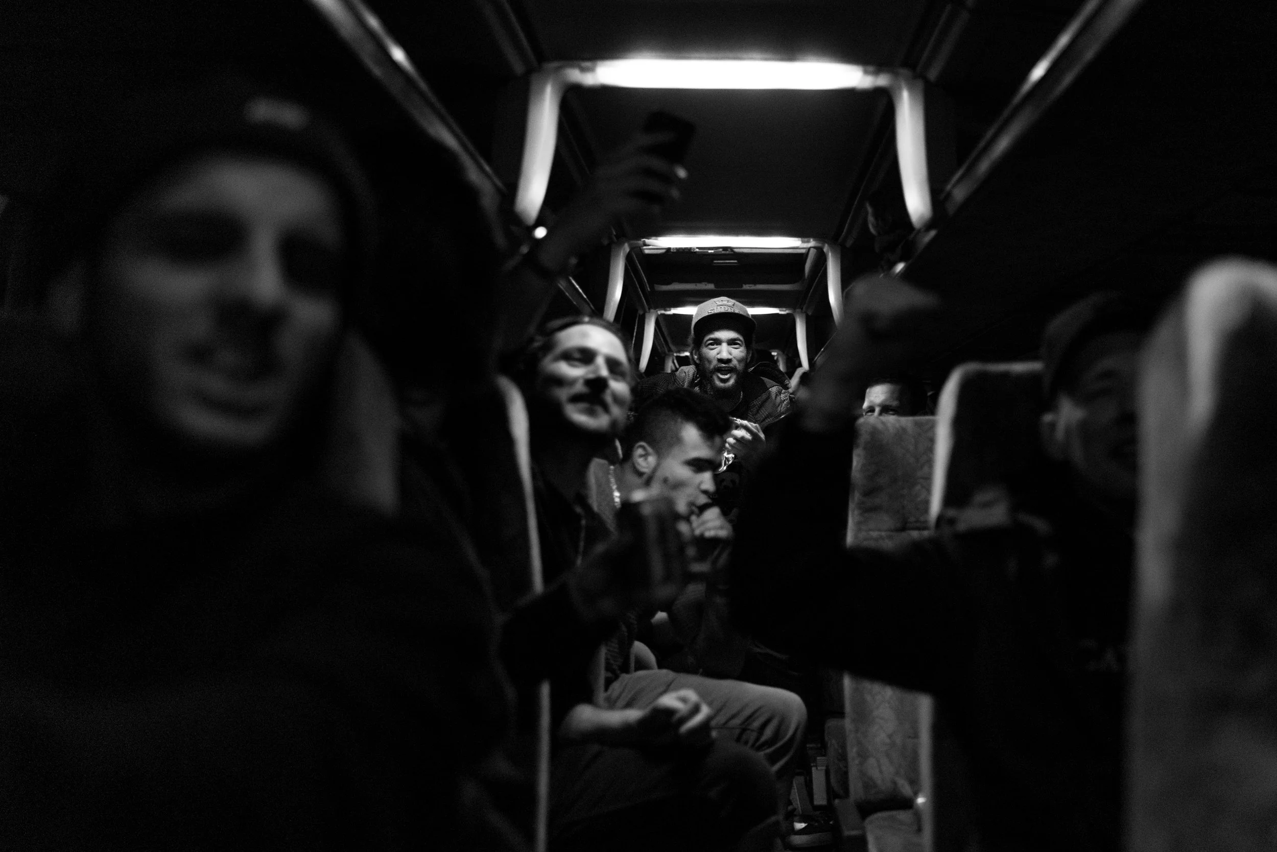 Groep mensen zittend op een bus, lachend en pratend, in een zwart-wit foto