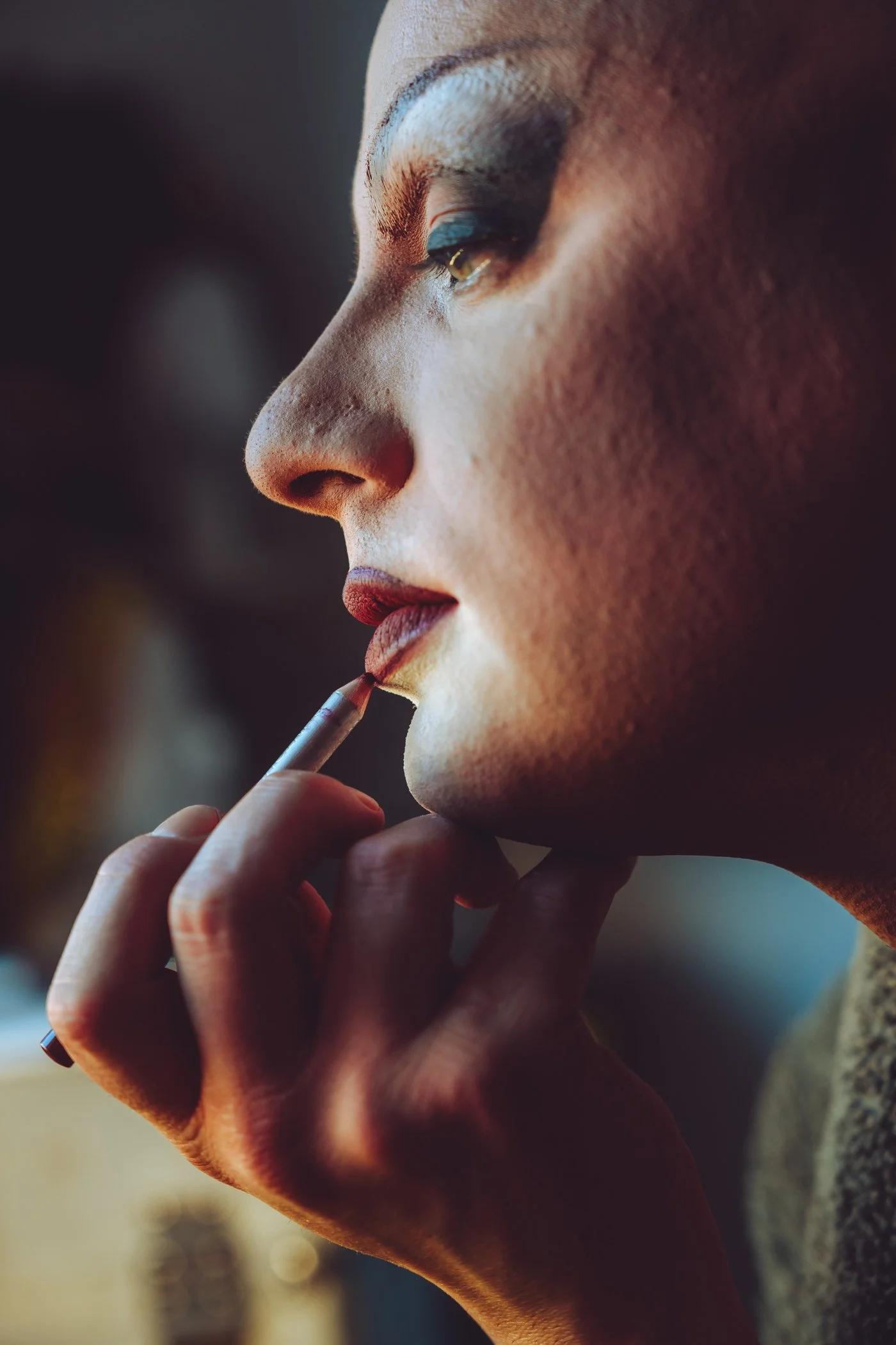 Close-up van een vrouw die lippenstift aanbrengt, met make-up en oogschaduw, terwijl ze haar kin ondersteunt met haar hand.