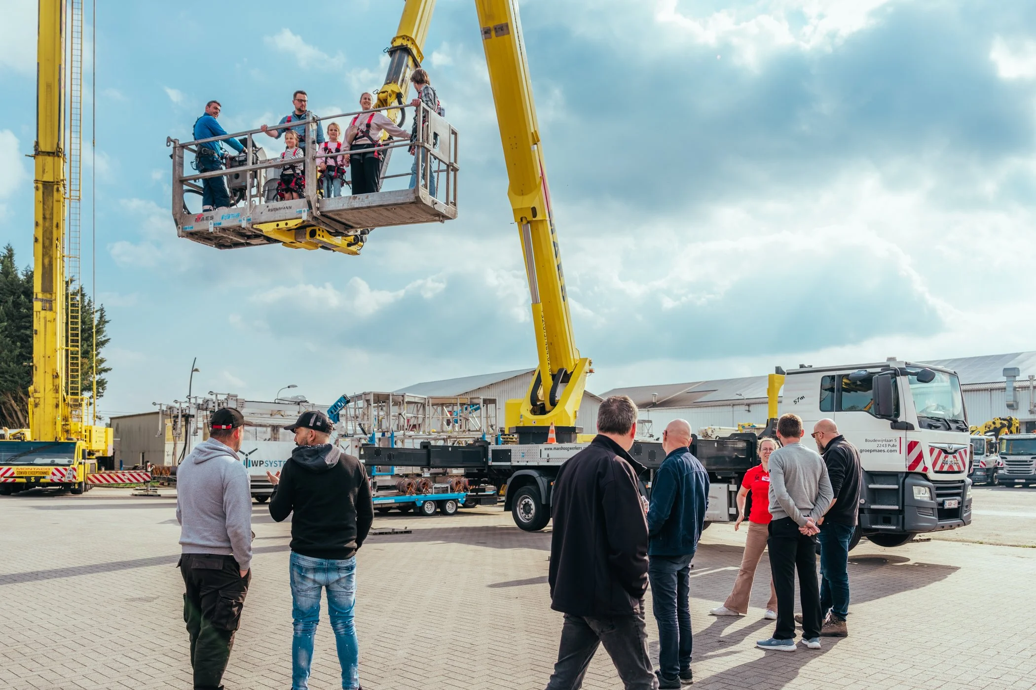 Groep mensen bekijken een demonstratie met een hoogwerker op een open terrein, onder een bewolkte hemel.