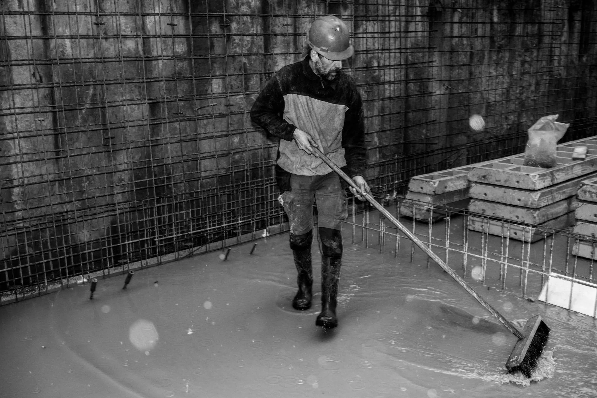 Lelijk geschilderde bouwvakker staat in een waterige bouwput en reinigt de vloer met een waterhopper.