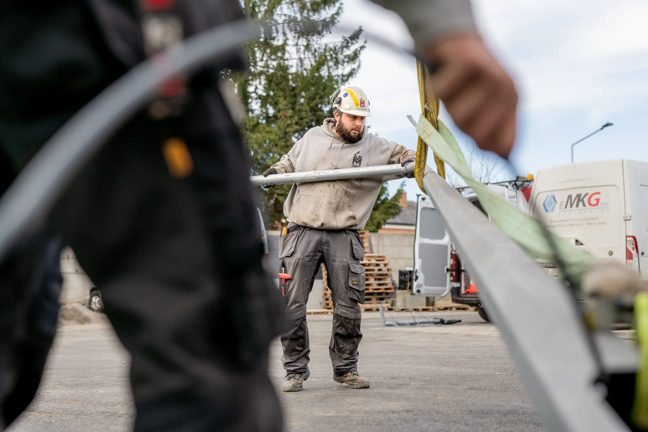 Arbeider die een veiligheidslijn of kabel inspecteert of vastzet, gezien vanaf een laag perspectief met andere uitrusting en voertuigen op de achtergrond.