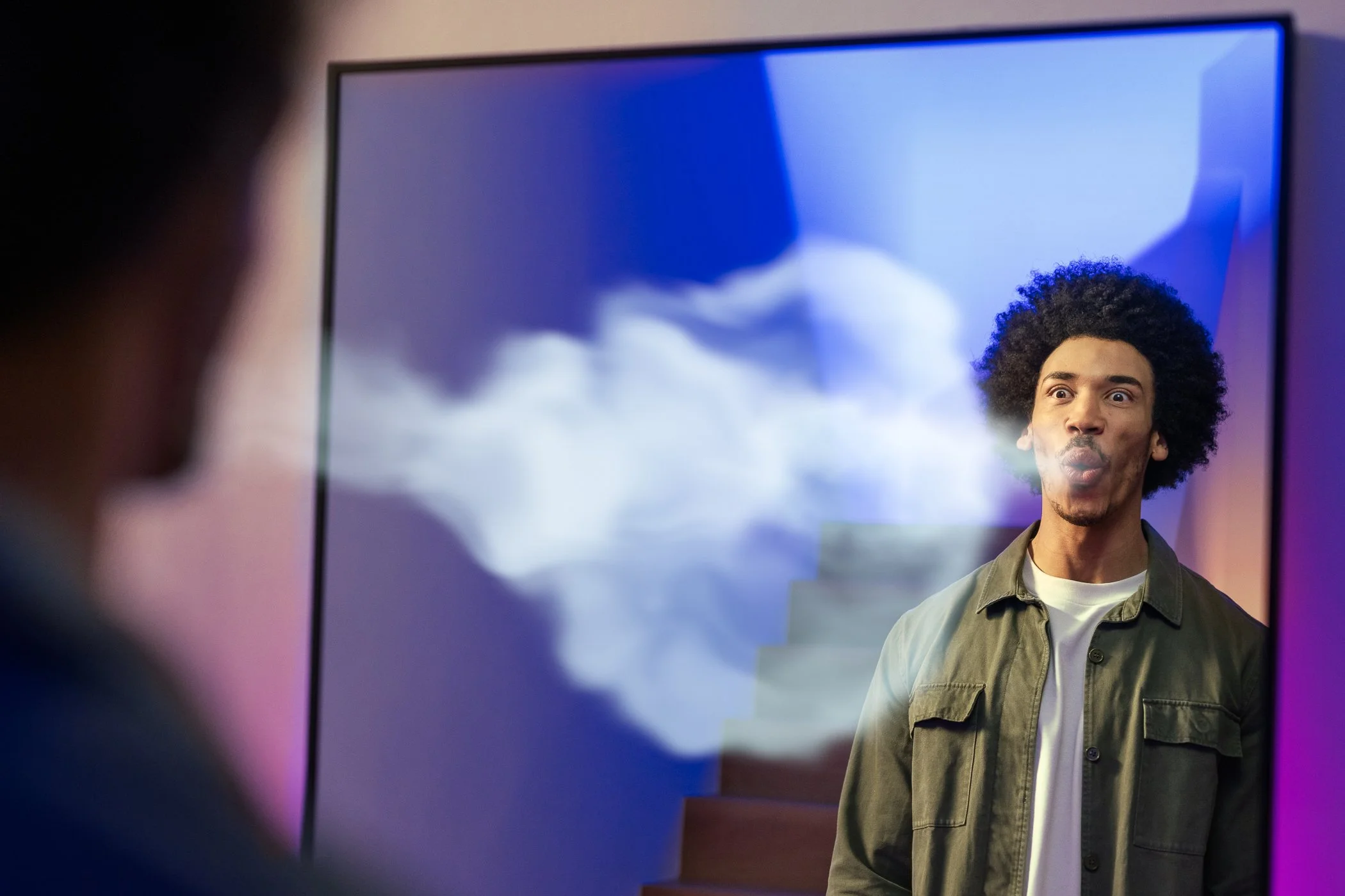 Een man met een afro haarstijl die rook uit zijn mond blaast terwijl hij in een mirror kijkt.