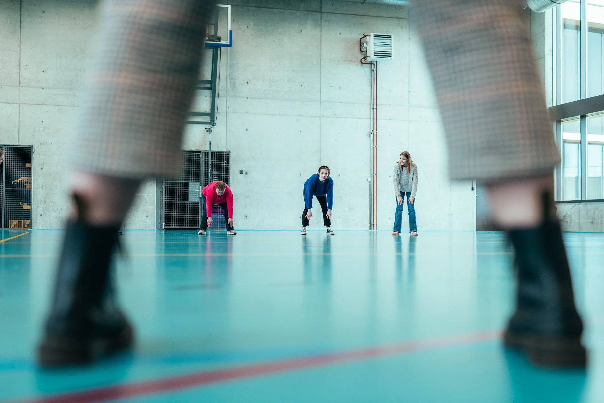 Vrouwen in een gymnastiekzaal die rekoefeningen doen, gezien vanuit een lage hoek door schoenen van een andere persoon.