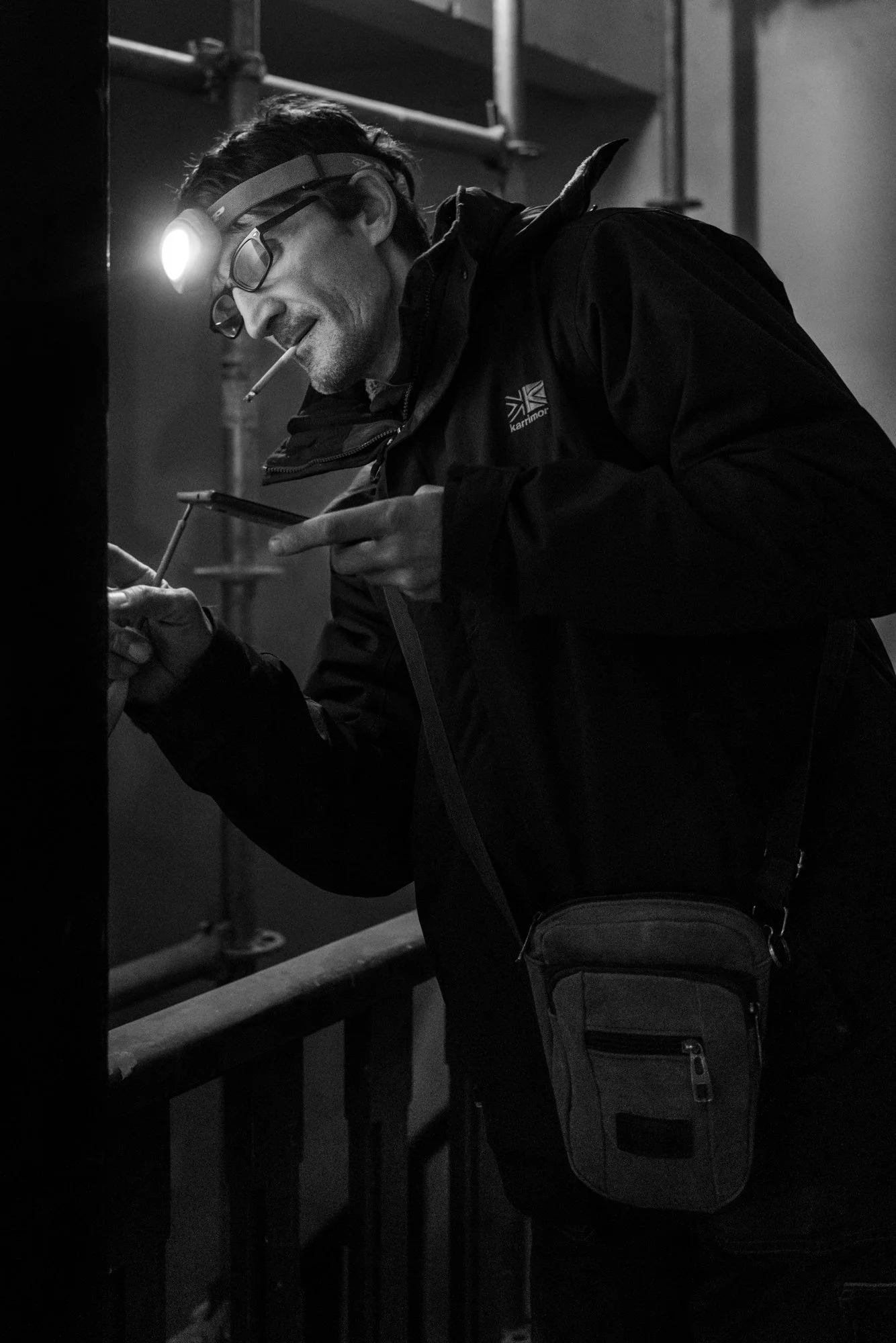 Man met bril en hoofdlamp schrijft op een muur in een donkere omgeving.