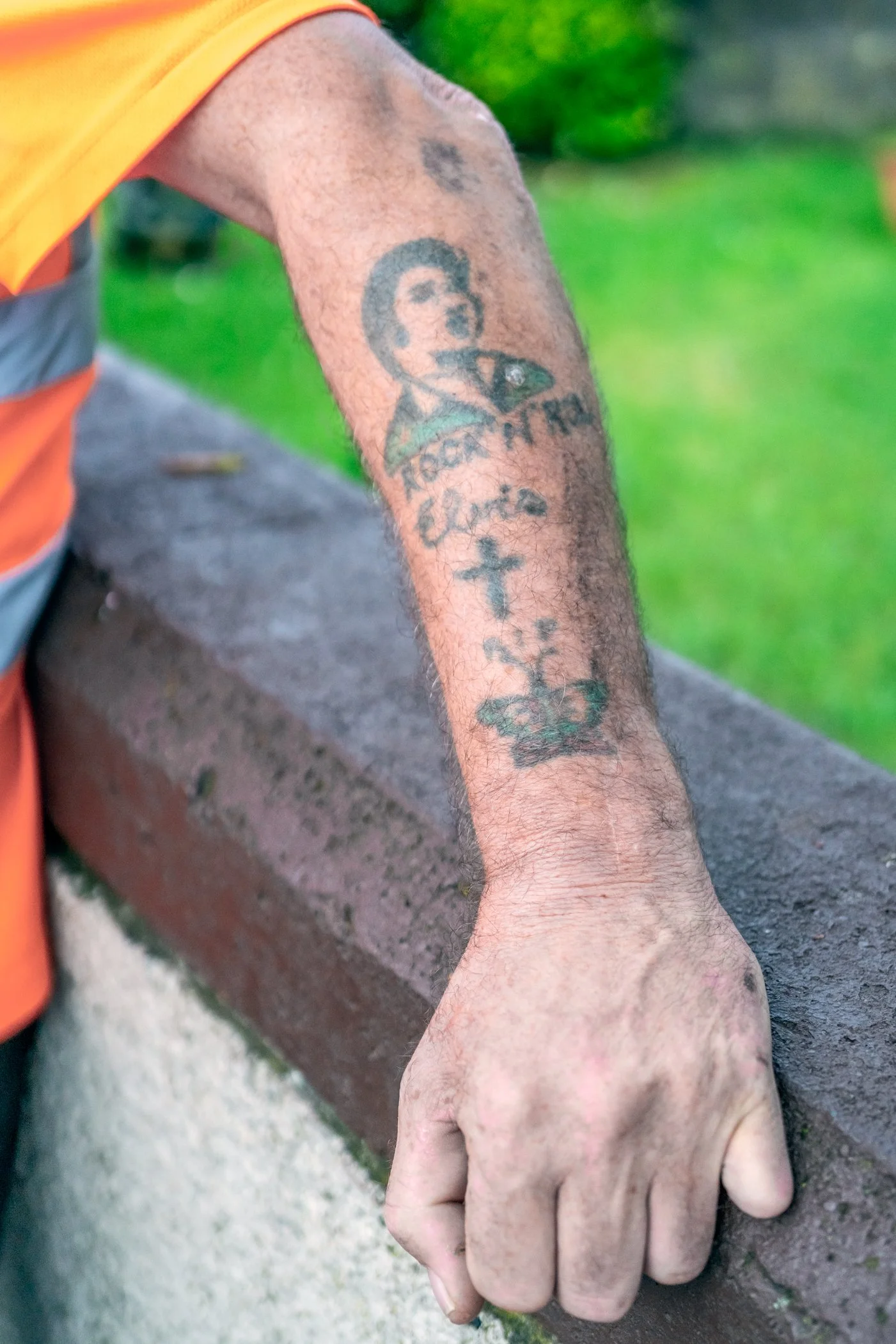 De bovenarm van een man met een tatoeage die een cartoonachtig gezicht, tekst, een kruis en een kroon bevat.