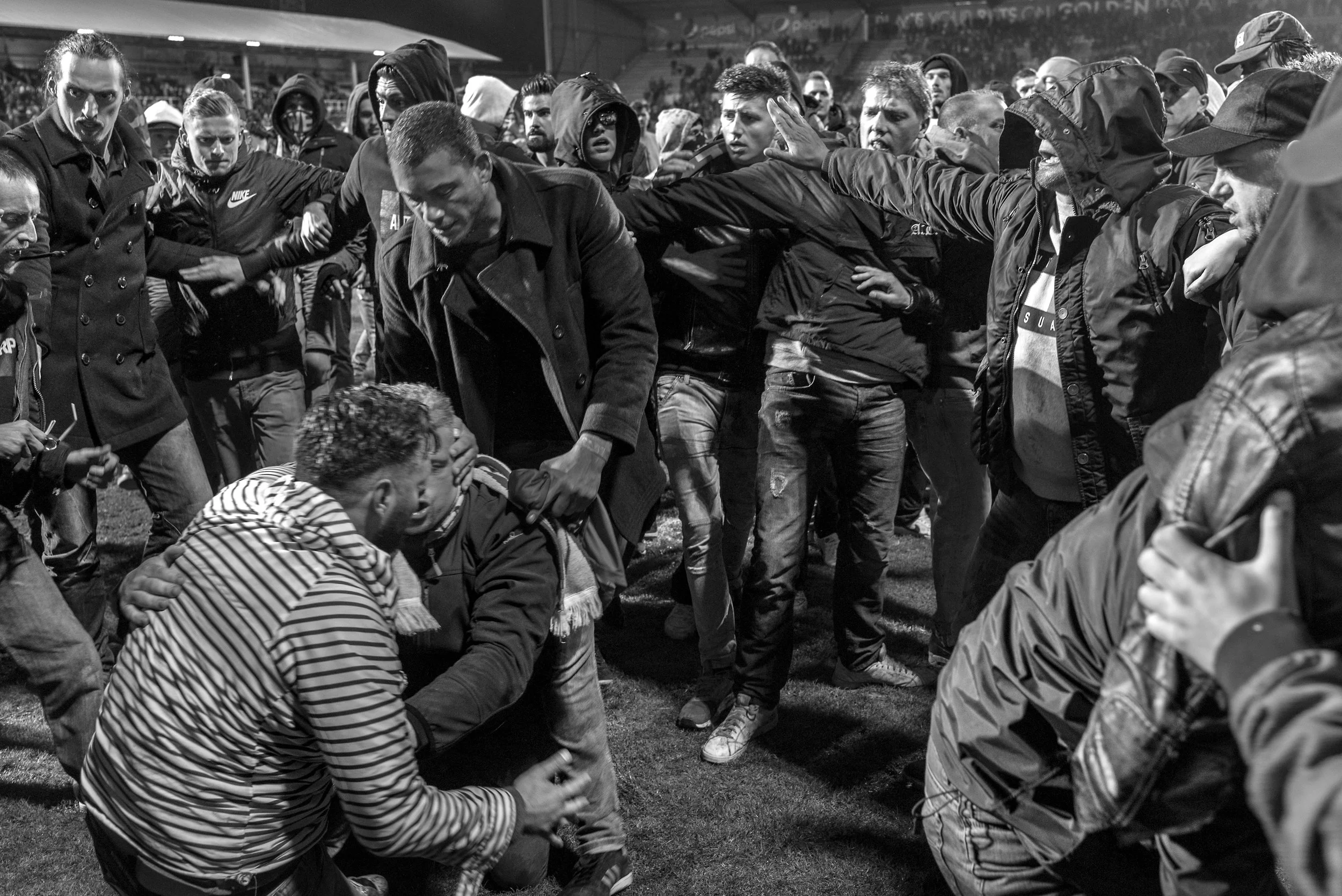 Een andere menigte mensen die tussen de rij staan, lijken te vechten of te worstelen, sommige mensen proberen anderen te kalmeren of te beschermen.